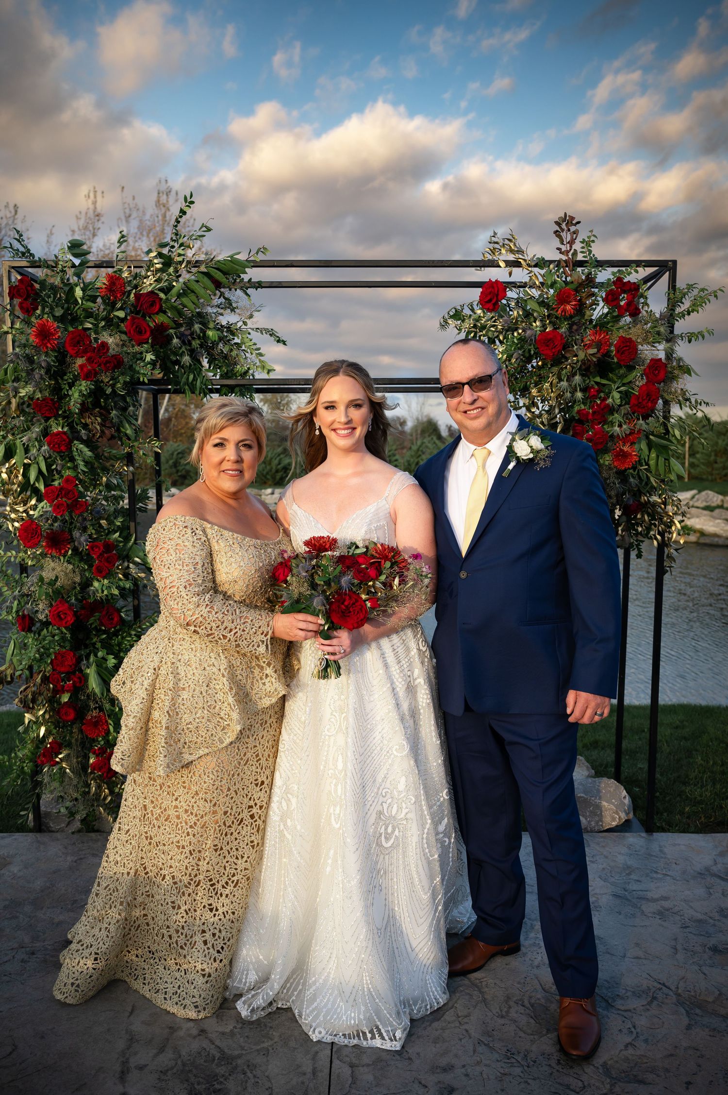 Wedding ceremony setup with red rose arch and waterfront view at sunset.