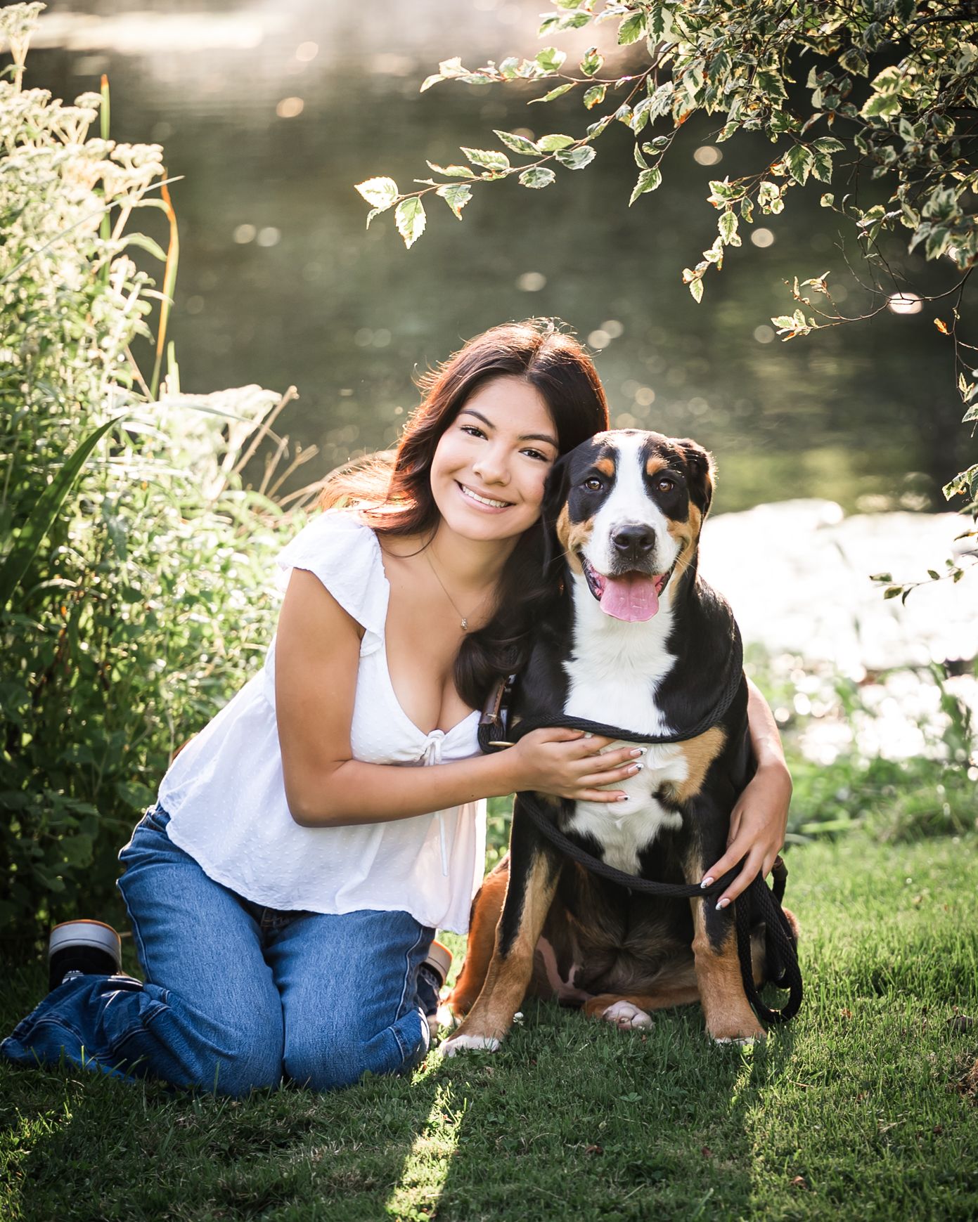 Woman in white shirt posing with happy Greater Swiss Mountain Dog by lakeside.