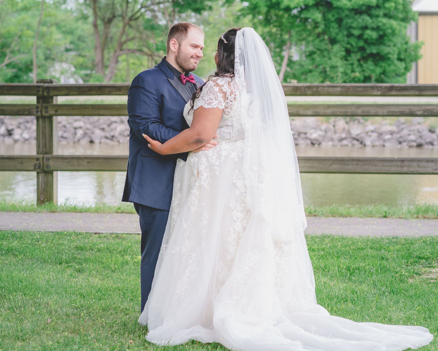 A bride and groom share an intimate moment by a rustic wooden fence during their outdoor wedding.