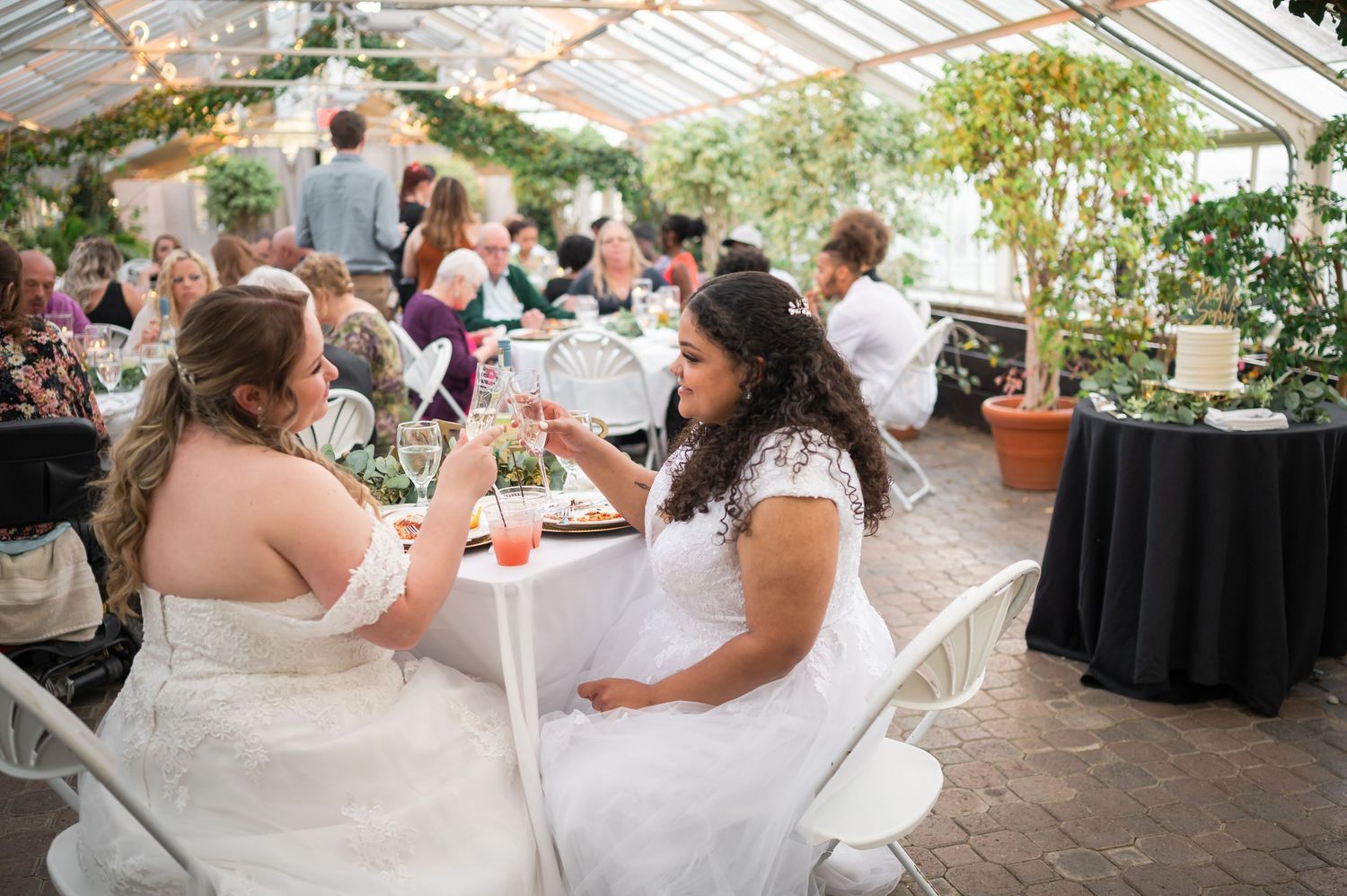 Wedding reception in a greenhouse with guests seated at tables surrounded by plants.