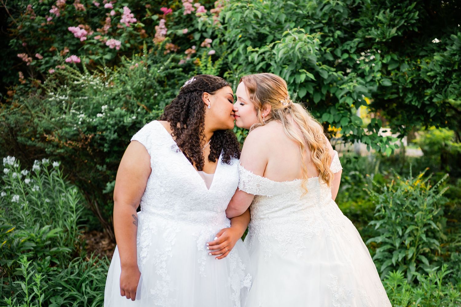 Intimate wedding moment captured in lush garden setting with white dresses.