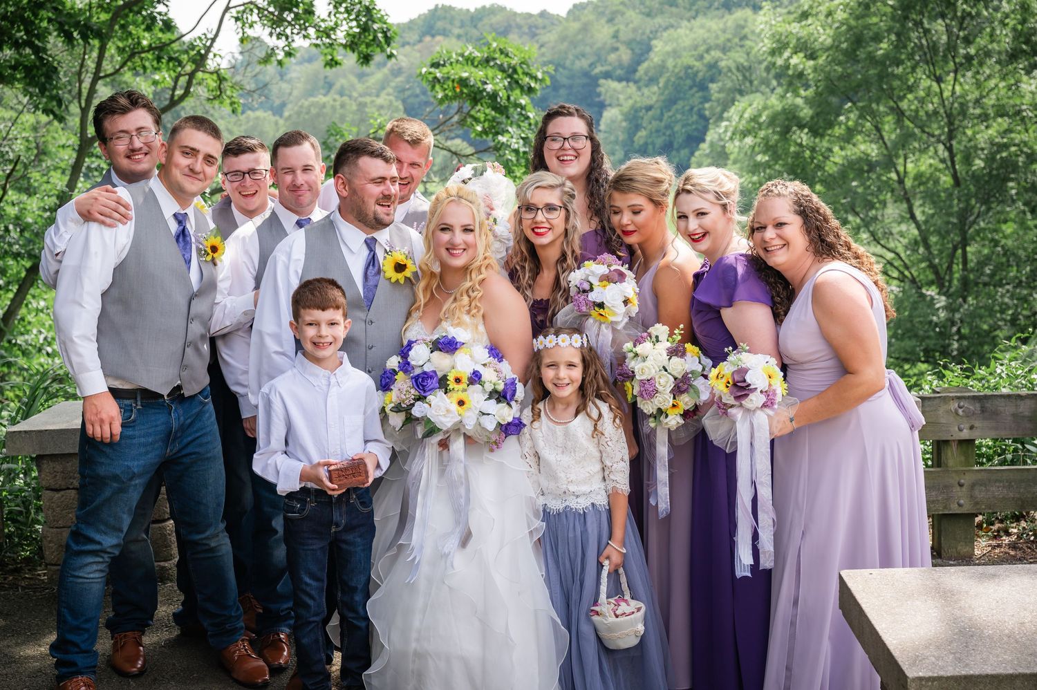 Wedding group photo with bridesmaids in purple, groomsmen in gray, and flower children in white.