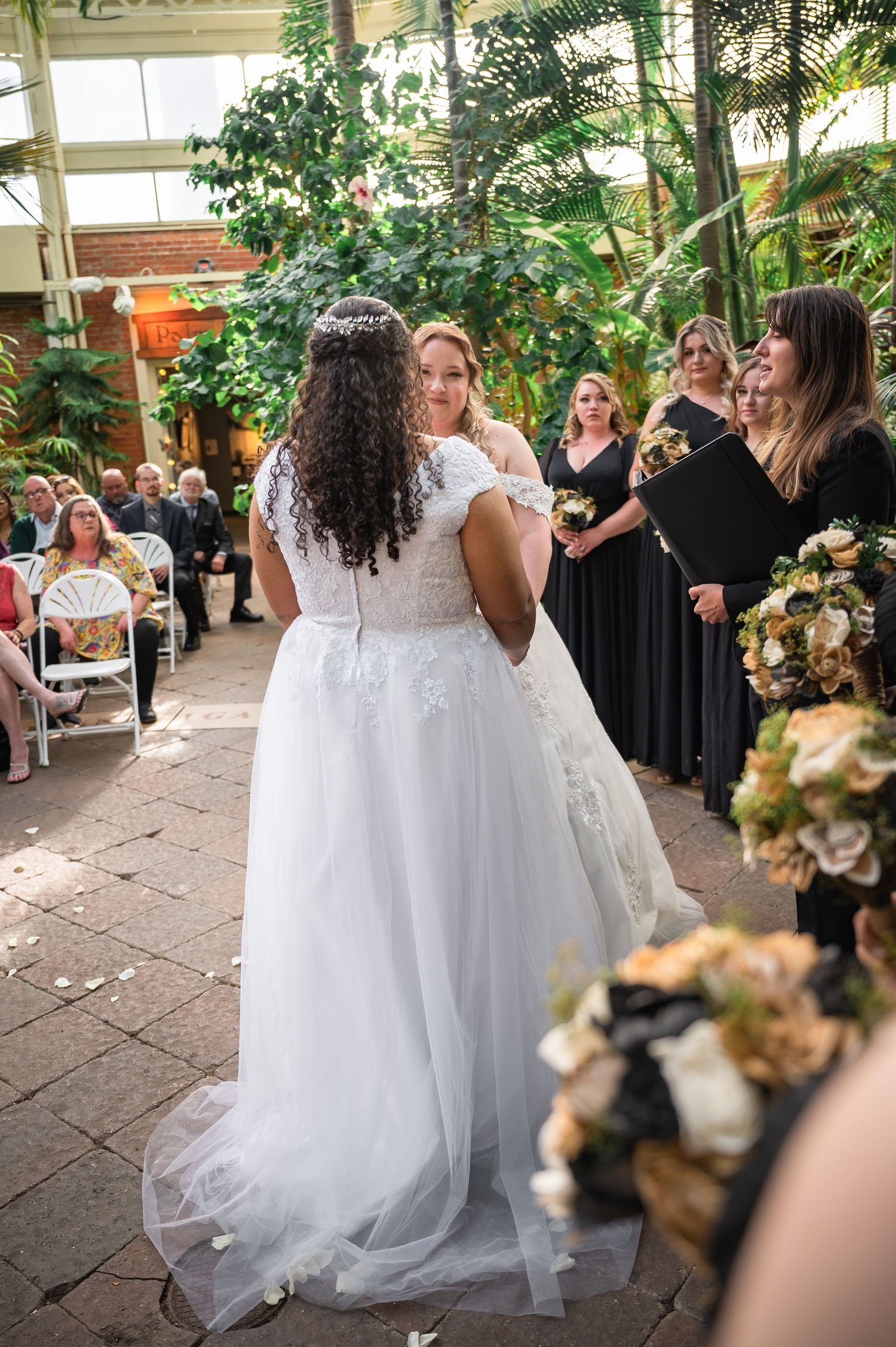Wedding celebration in a conservatory with bridal party and guests in formal attire.