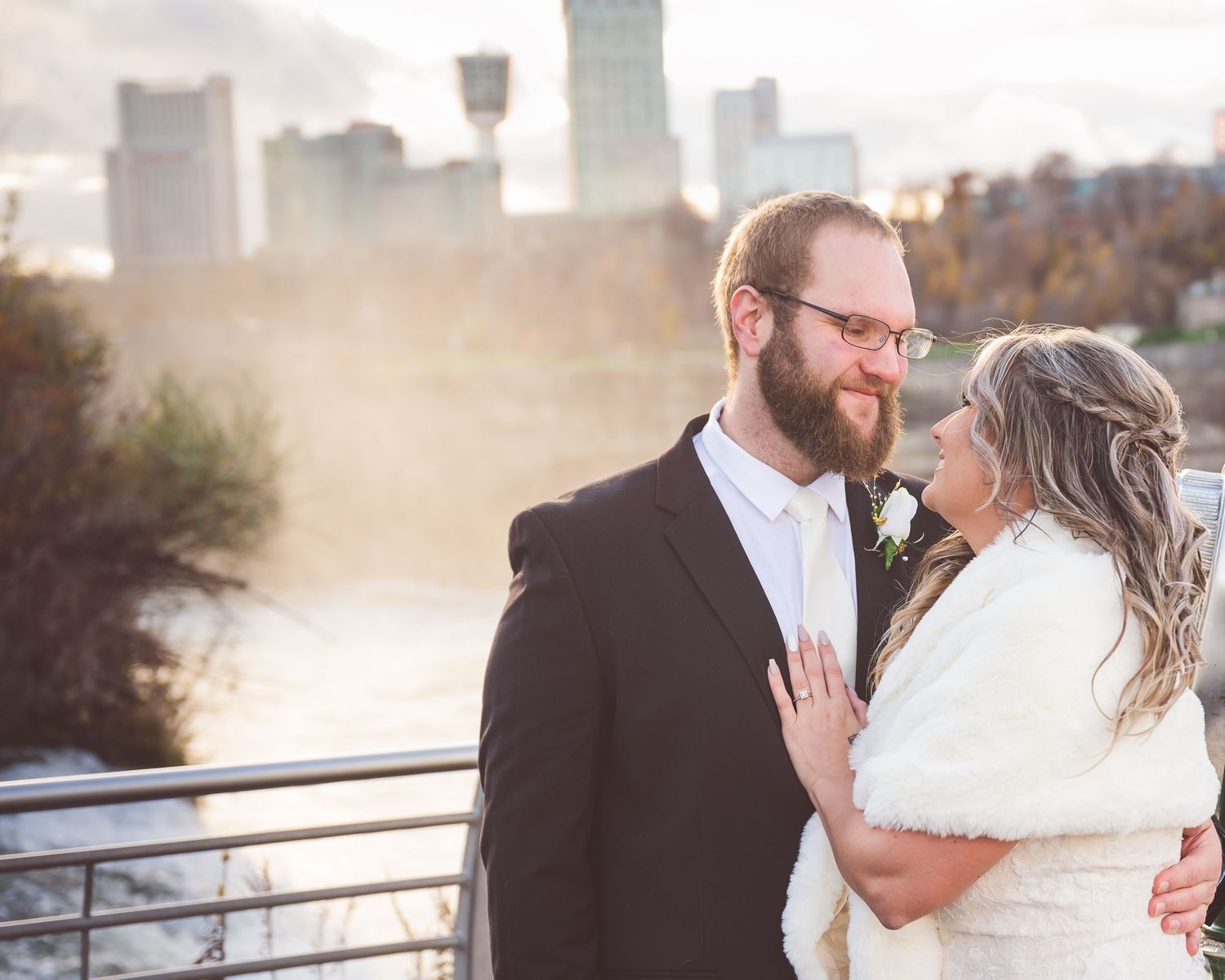 Romantic sunset wedding portrait on riverside deck with city skyline in background.