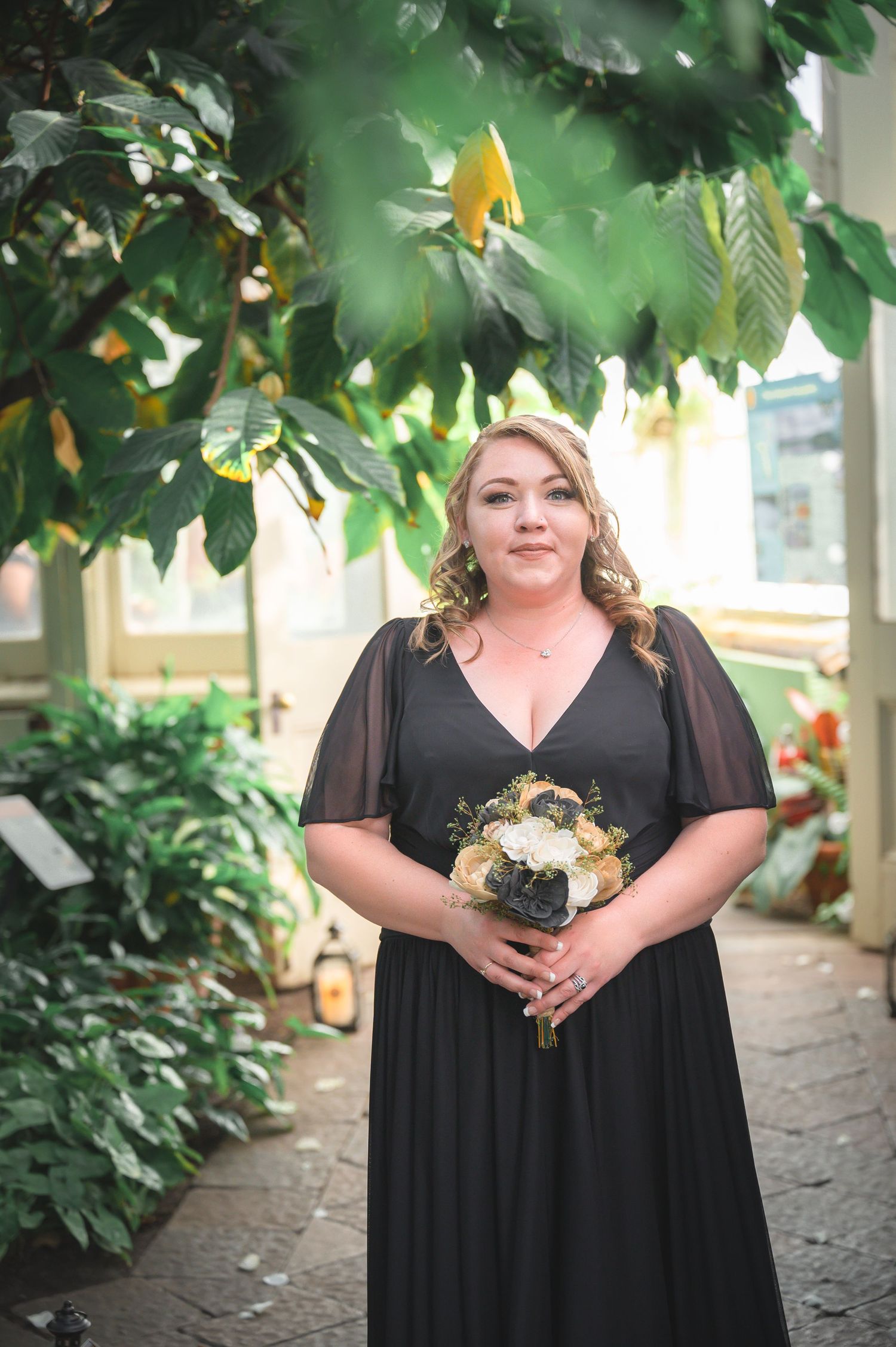 Formal black dress worn in a lush conservatory setting with tropical plants.