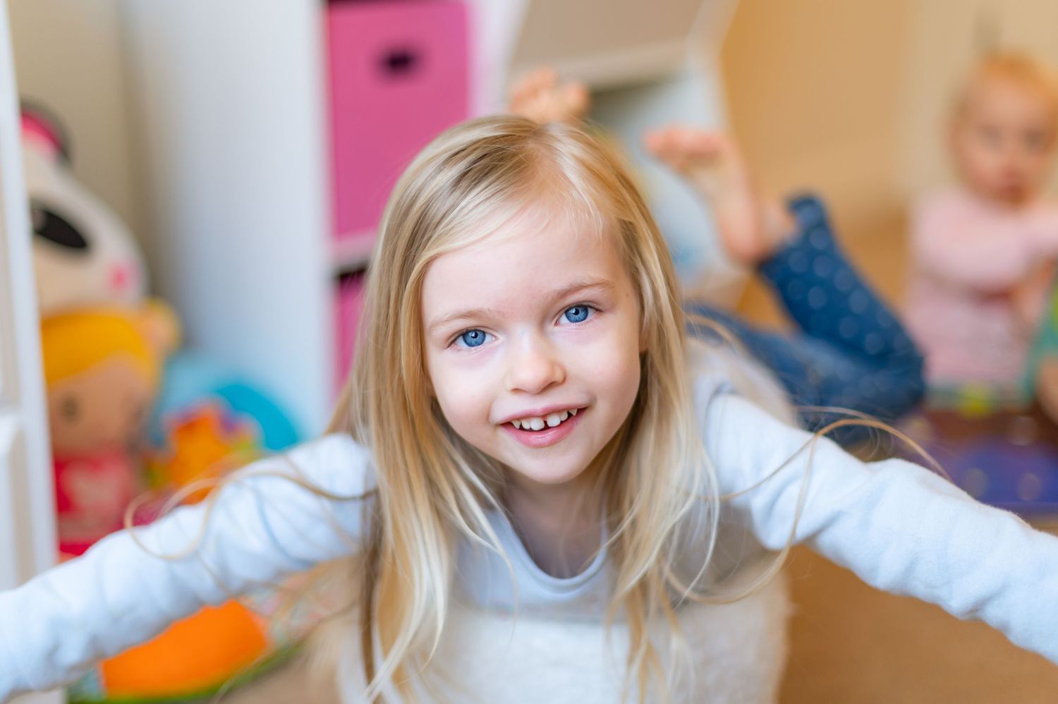 Child playing and smiling in playroom surrounded by toys.