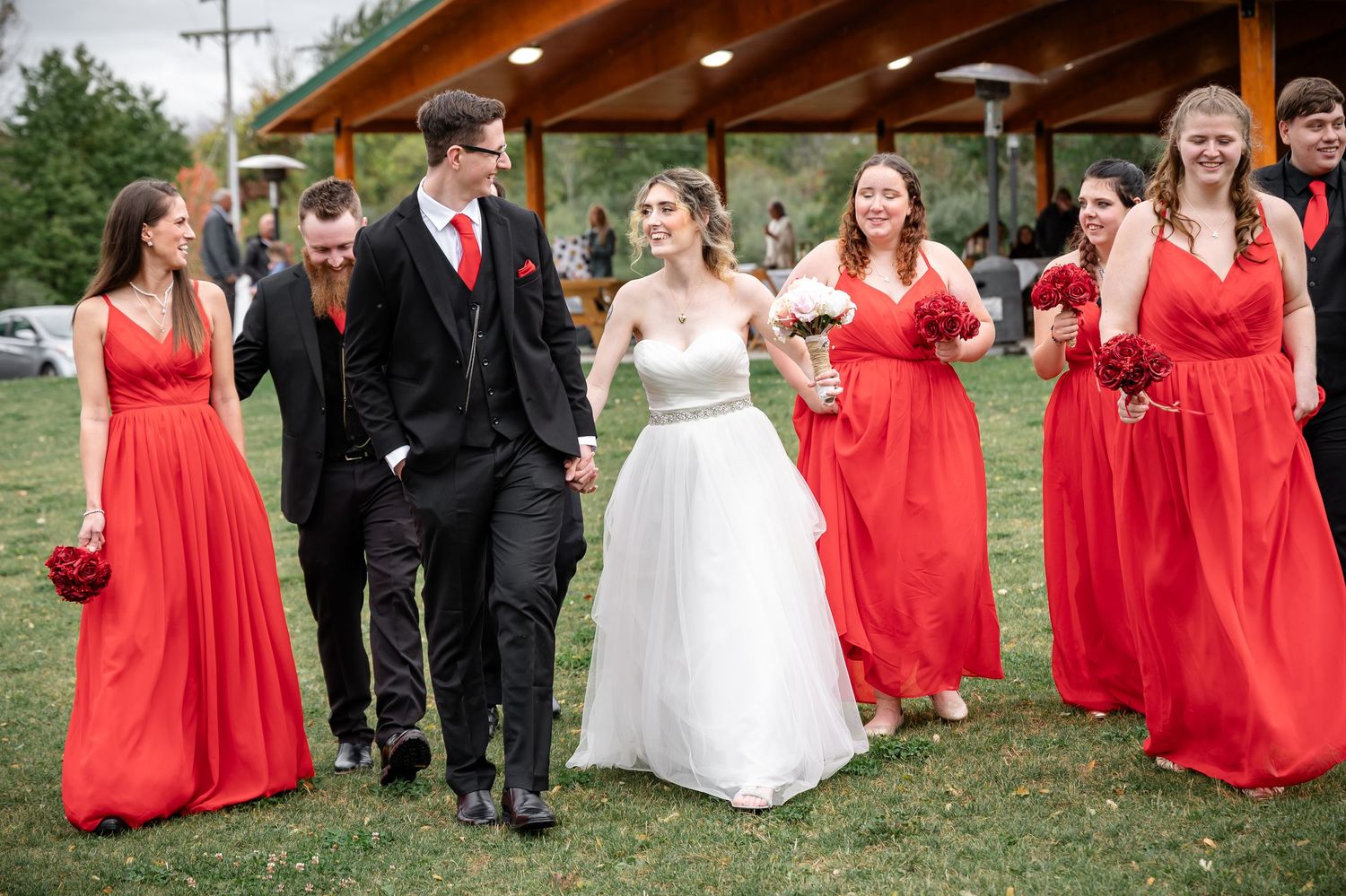 Wedding party walks together outside with bridesmaids in vibrant red dresses.