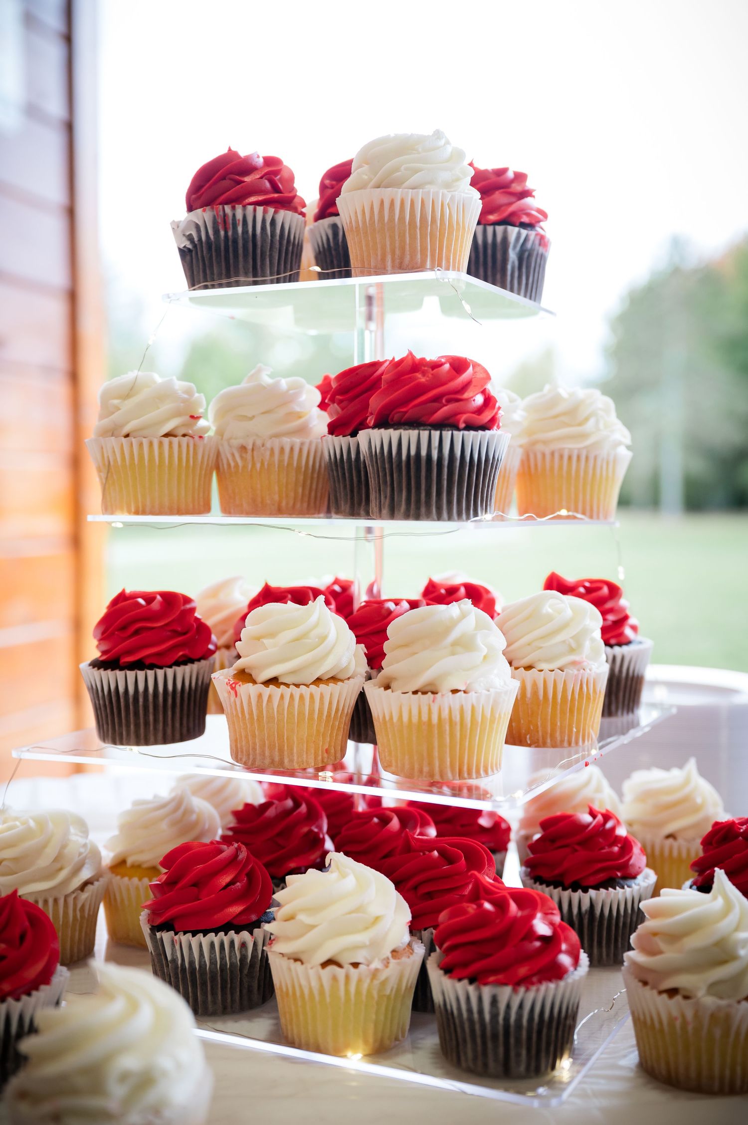 Tiered display of red and white frosted cupcakes at wedding reception.
