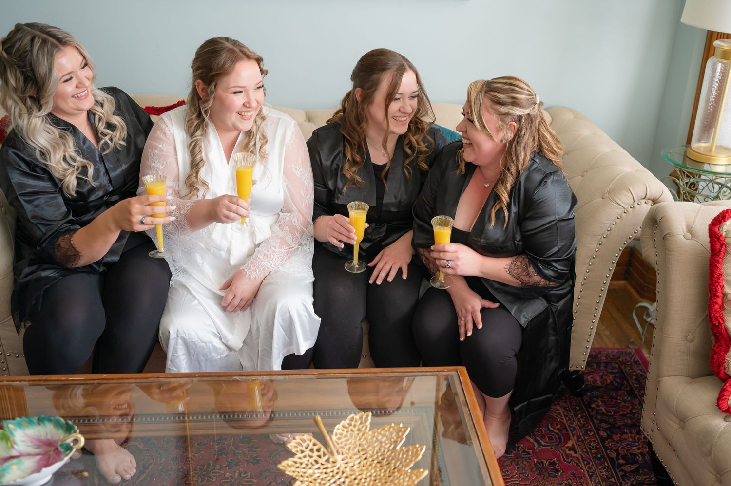 Bridal party sharing drinks and laughter while seated around a decorative coffee table.