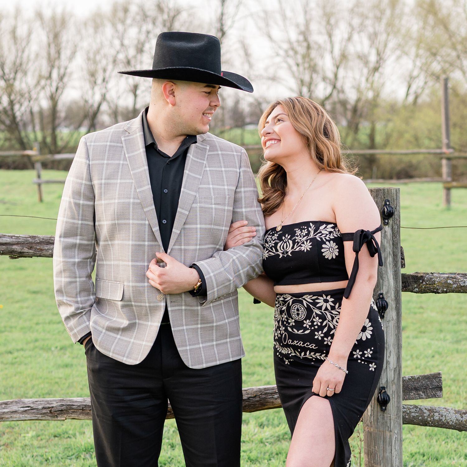 A romantic couple shares a laugh while posing by a rustic fence on a spring day.