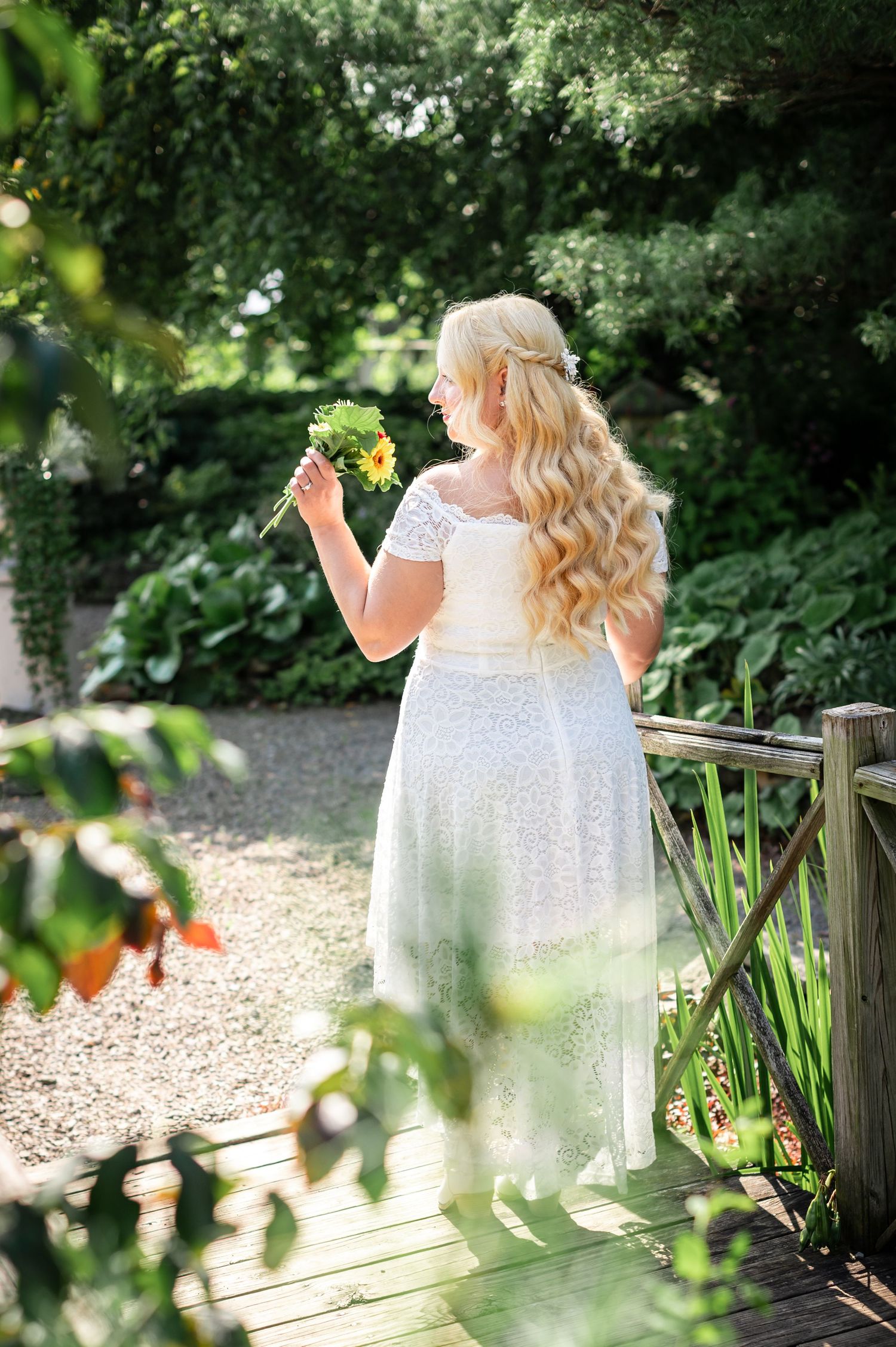 Dreamy garden scene with person holding flowers on wooden bridge.