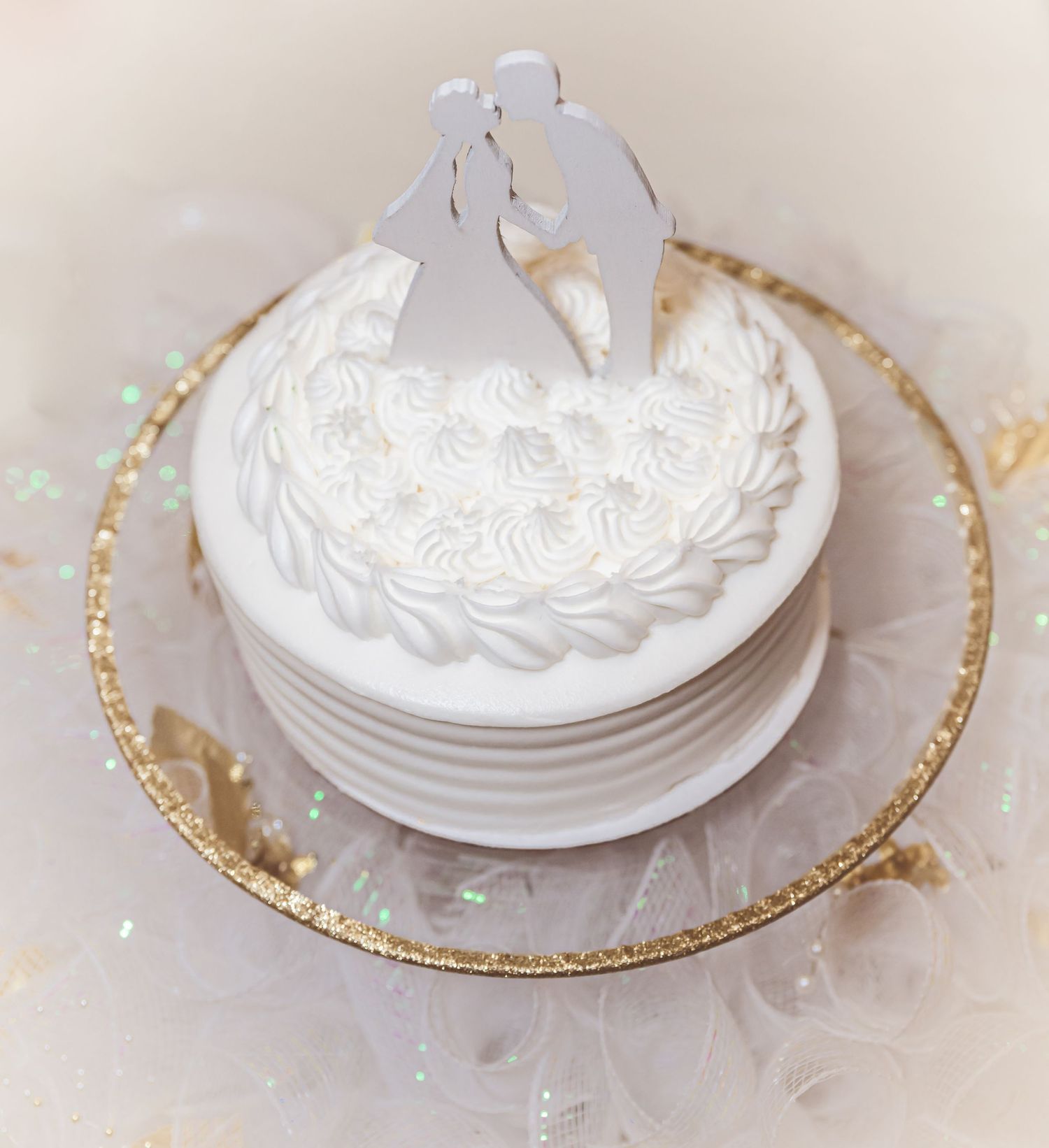 A white wedding cake decorated with frosting swirls and topped with a romantic silhouette cake topper.