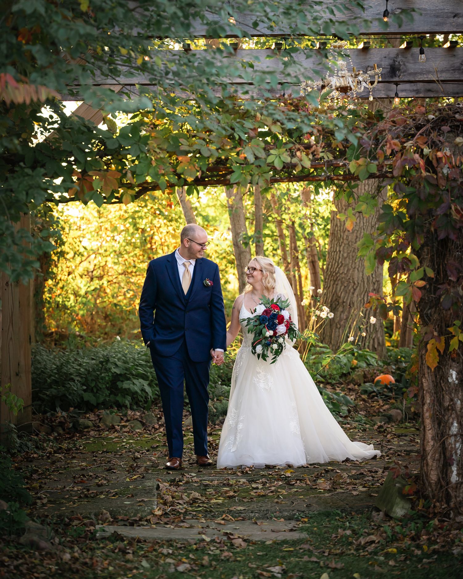 A couple shares an intimate autumn wedding moment beneath a wooden pergola in a sunlit garden setting.