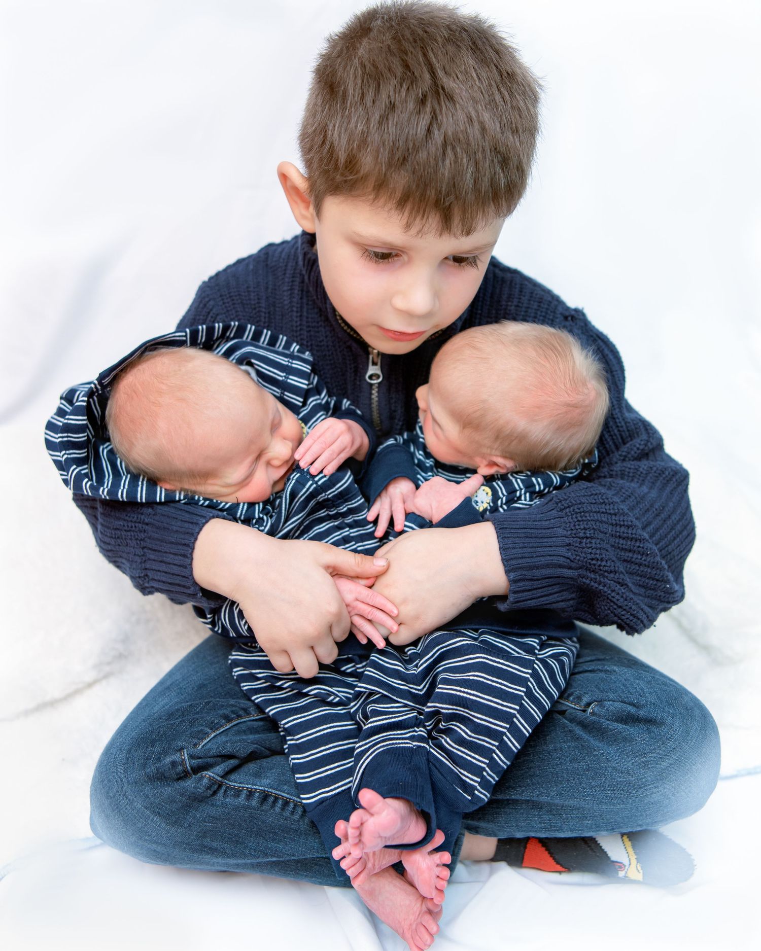 Child in striped shirt and jeans curled up on white background.