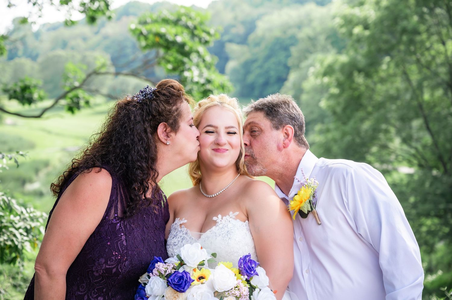 Sweet moment captured as the bride receives kisses on her cheeks while holding a blue and white bouquet.