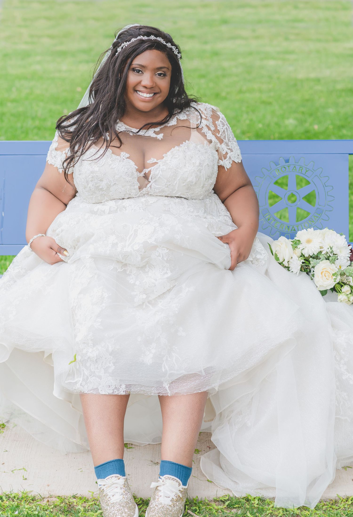 Bride in lace gown and blue socks sits on bench with flowing white dress.