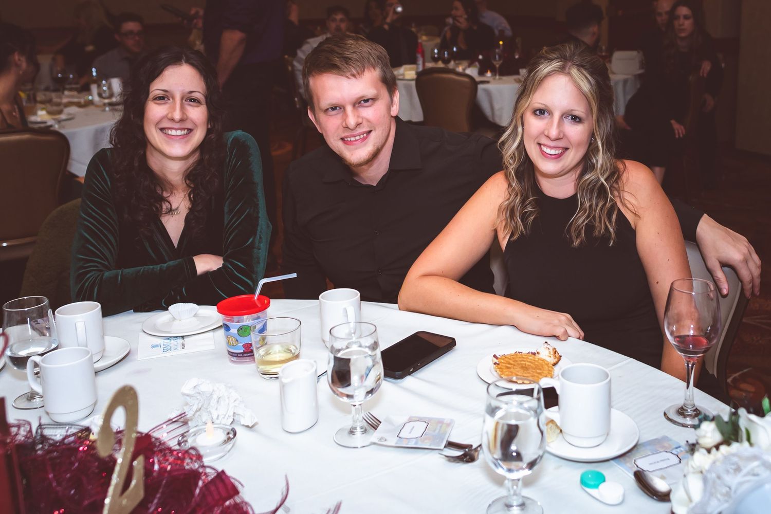 Three friends enjoying dinner together at an elegant banquet table setting with white tablecloths and place settings.