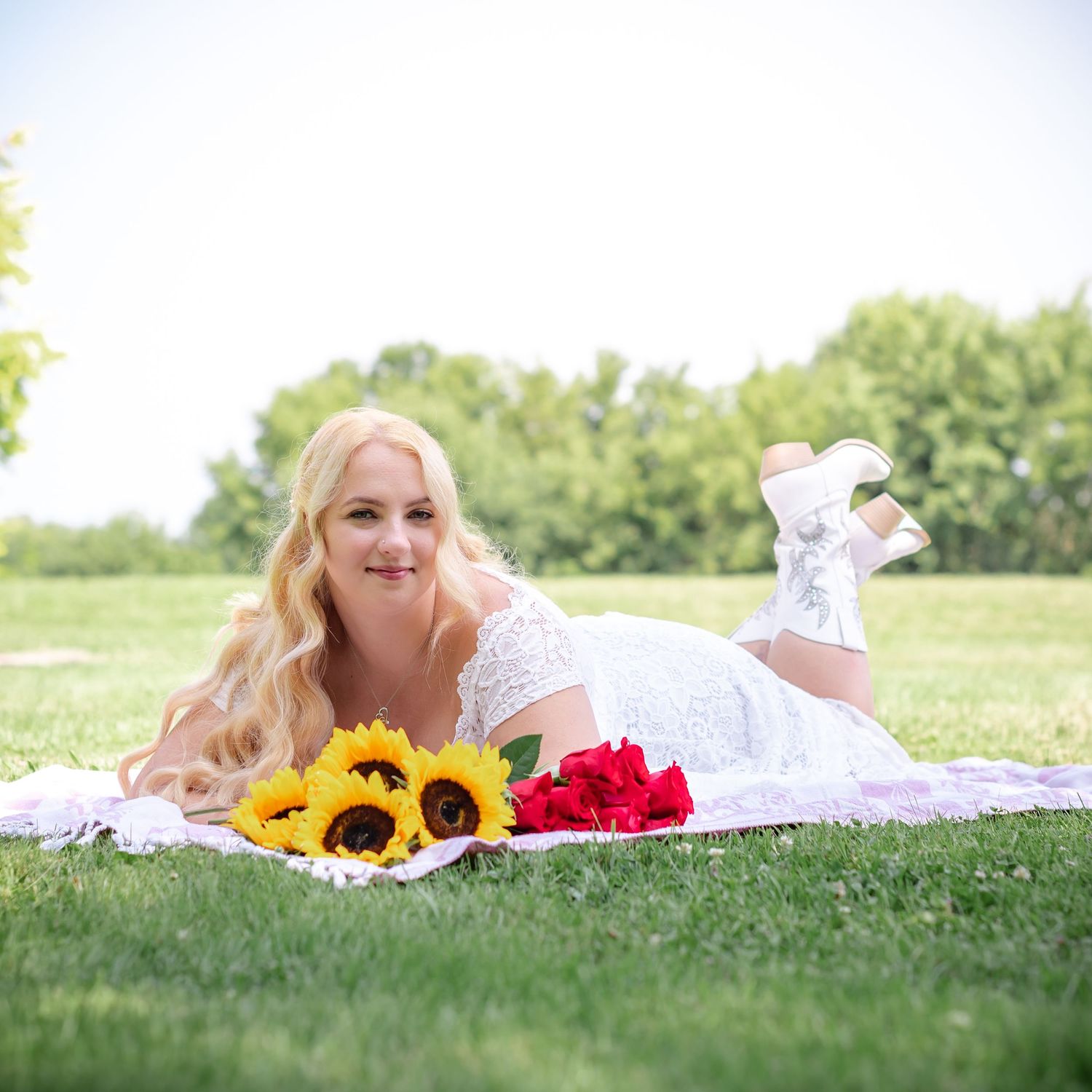 White lace dress on picnic blanket with sunflowers and roses in sunny garden setting.