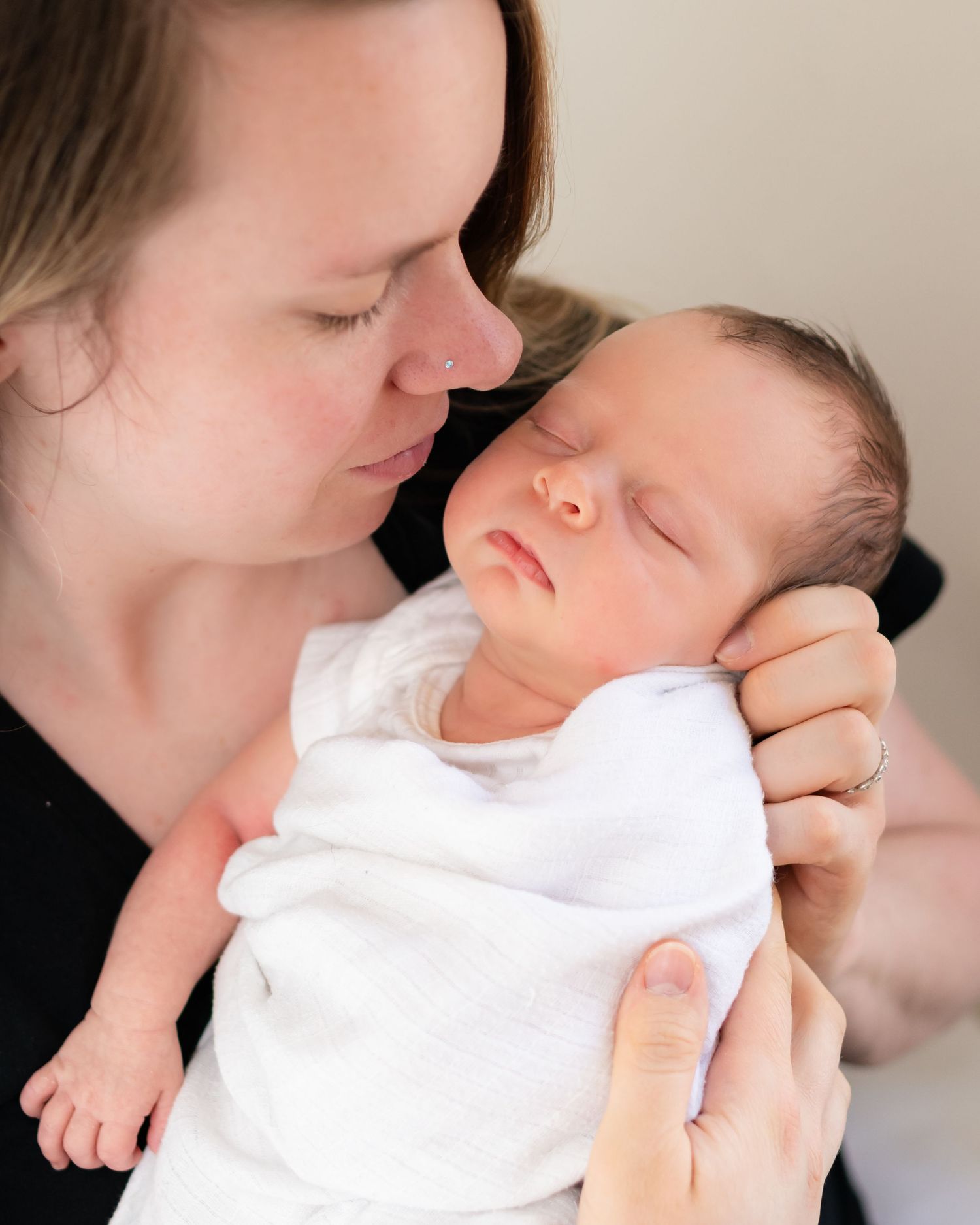 Intimate close-up portraits showing gentle moments between a parent and newborn dressed in white.