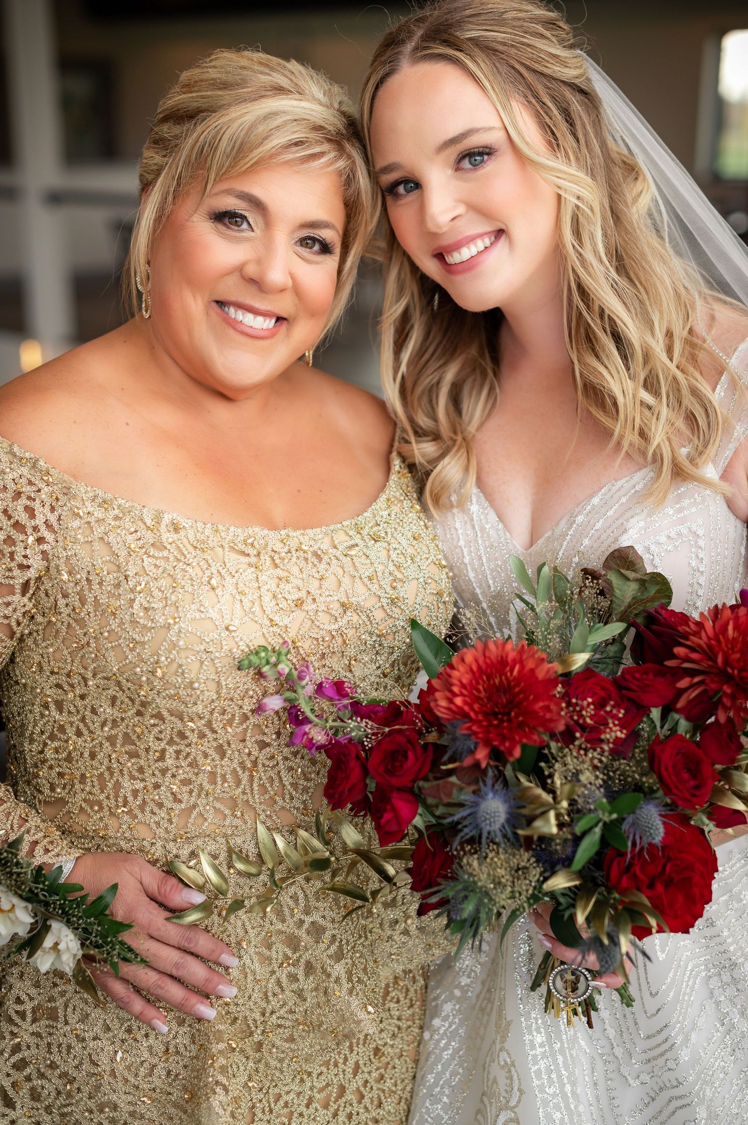 Elegant wedding photo featuring a gold lace gown and white bridal dress with stunning red and burgundy floral bouquet.