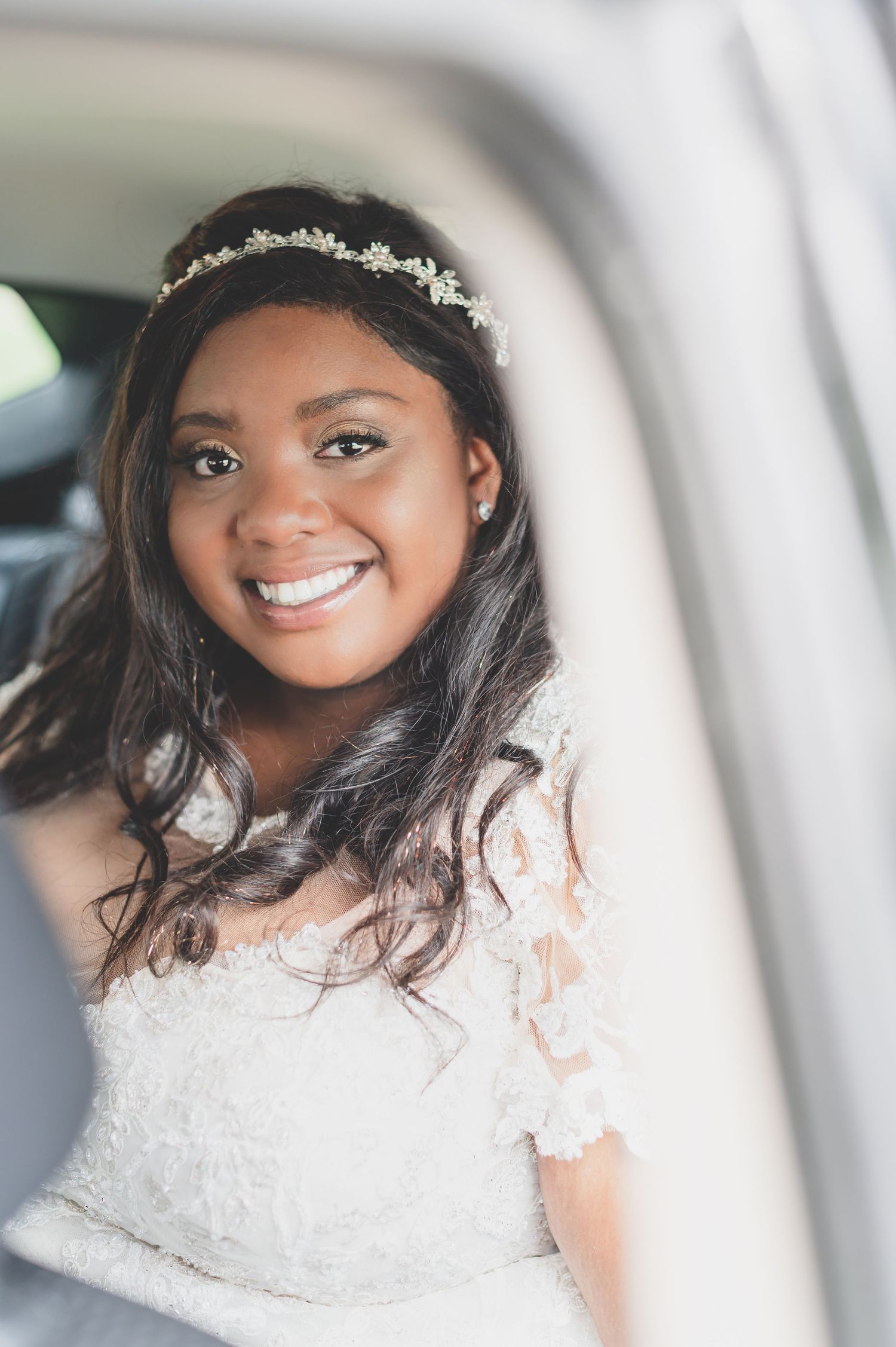 A beautiful bride wearing a delicate tiara and lace dress poses in a car.