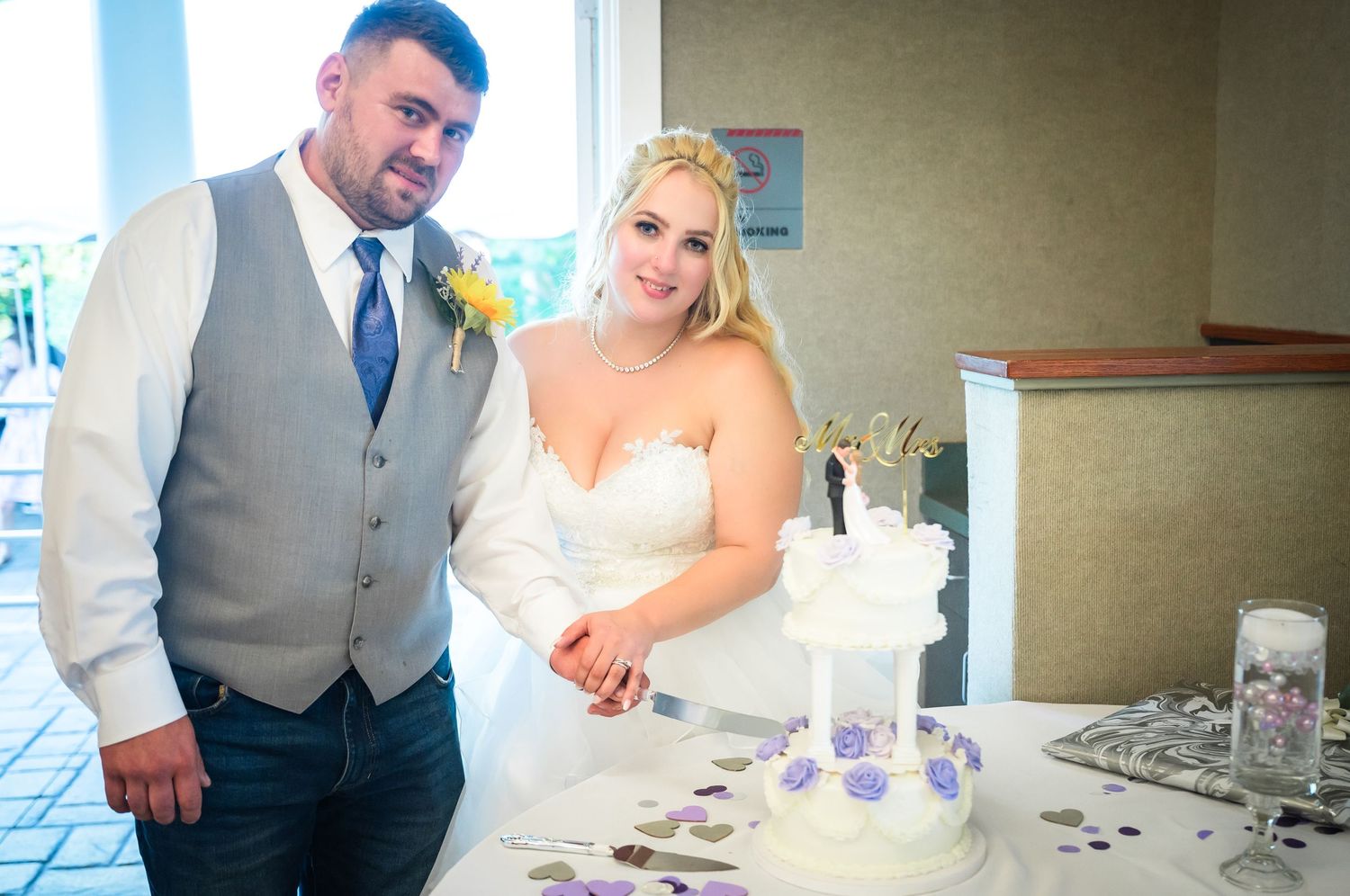A couple cutting their purple and white wedding cake together at their reception.