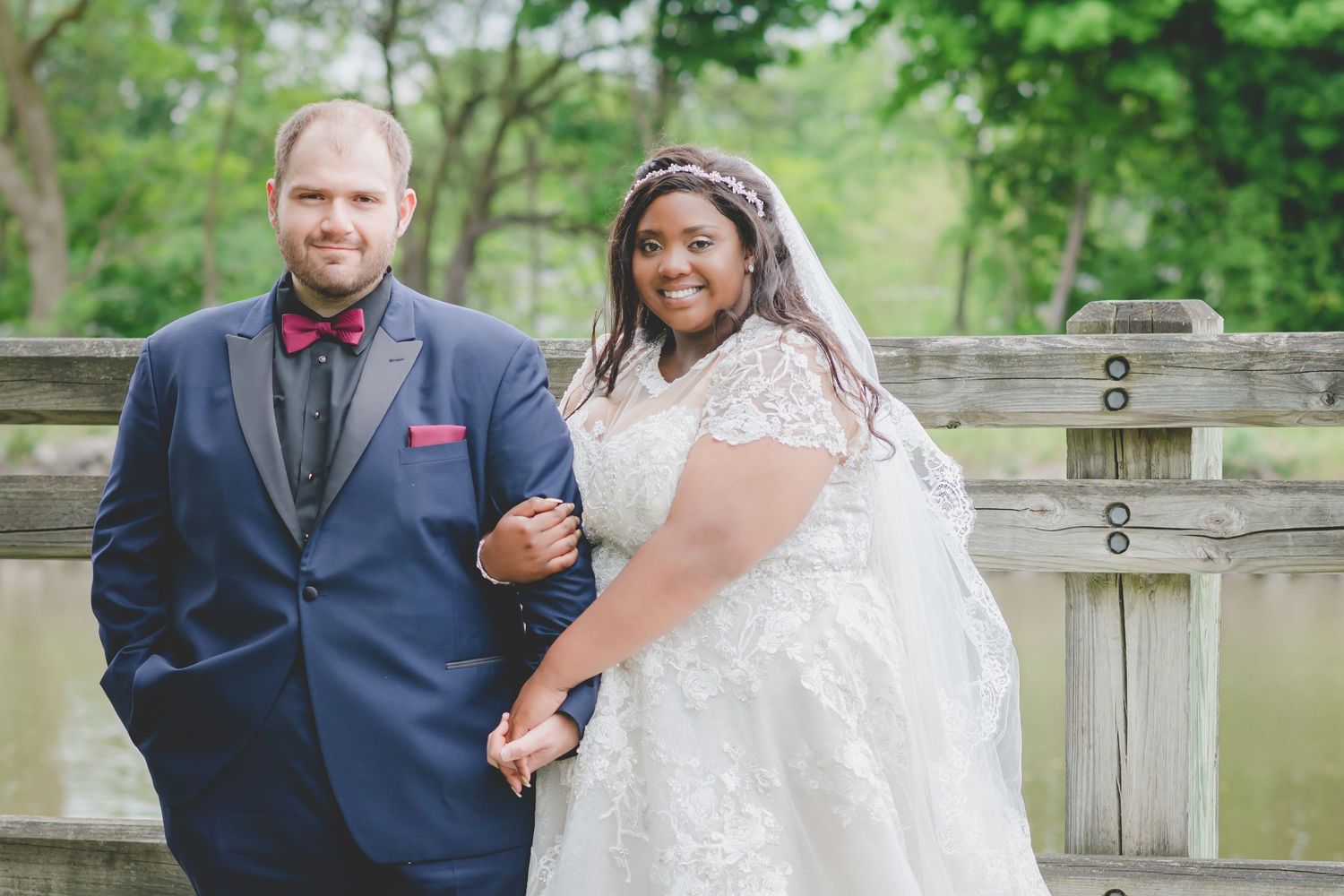 A joyful wedding couple poses outdoors near a wooden railing on their special day.