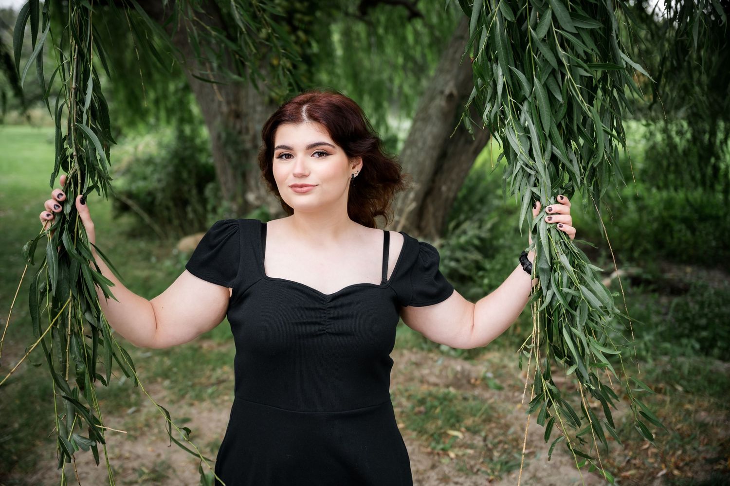 Holding willow branches while wearing a black dress in a garden setting.