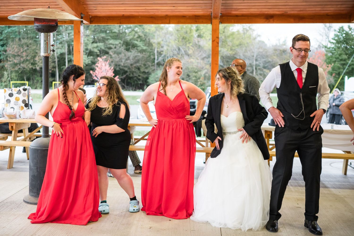 Wedding party in red and black attire dancing at indoor reception venue.