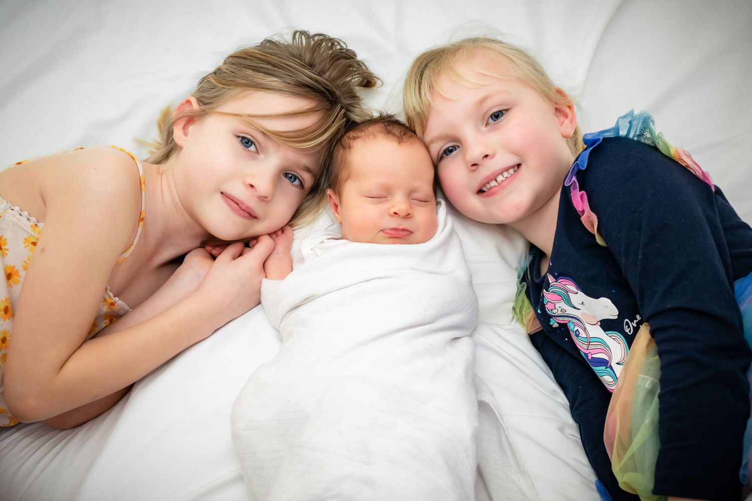 A heartwarming series of photos showing siblings bonding with a newborn baby on white bedding.