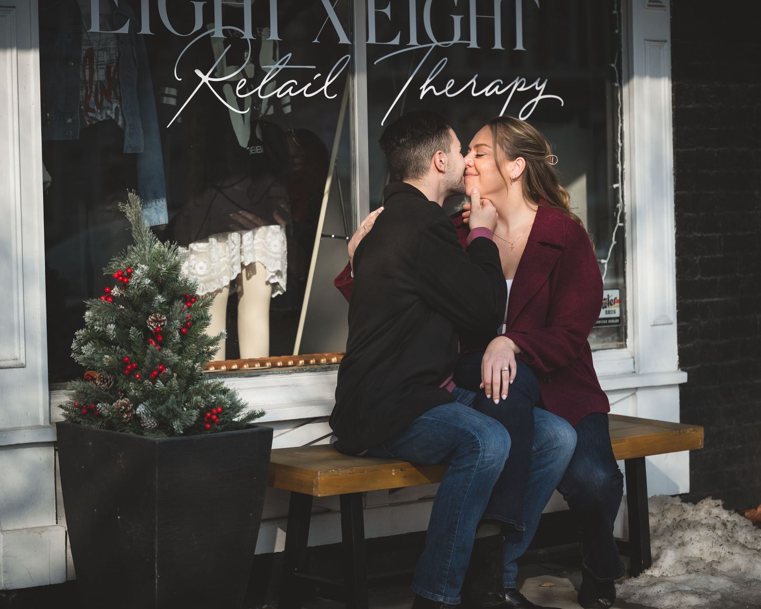 Couple sharing a kiss on a bench outside Eight Eight Retail Therapy shop with festive Christmas decor.