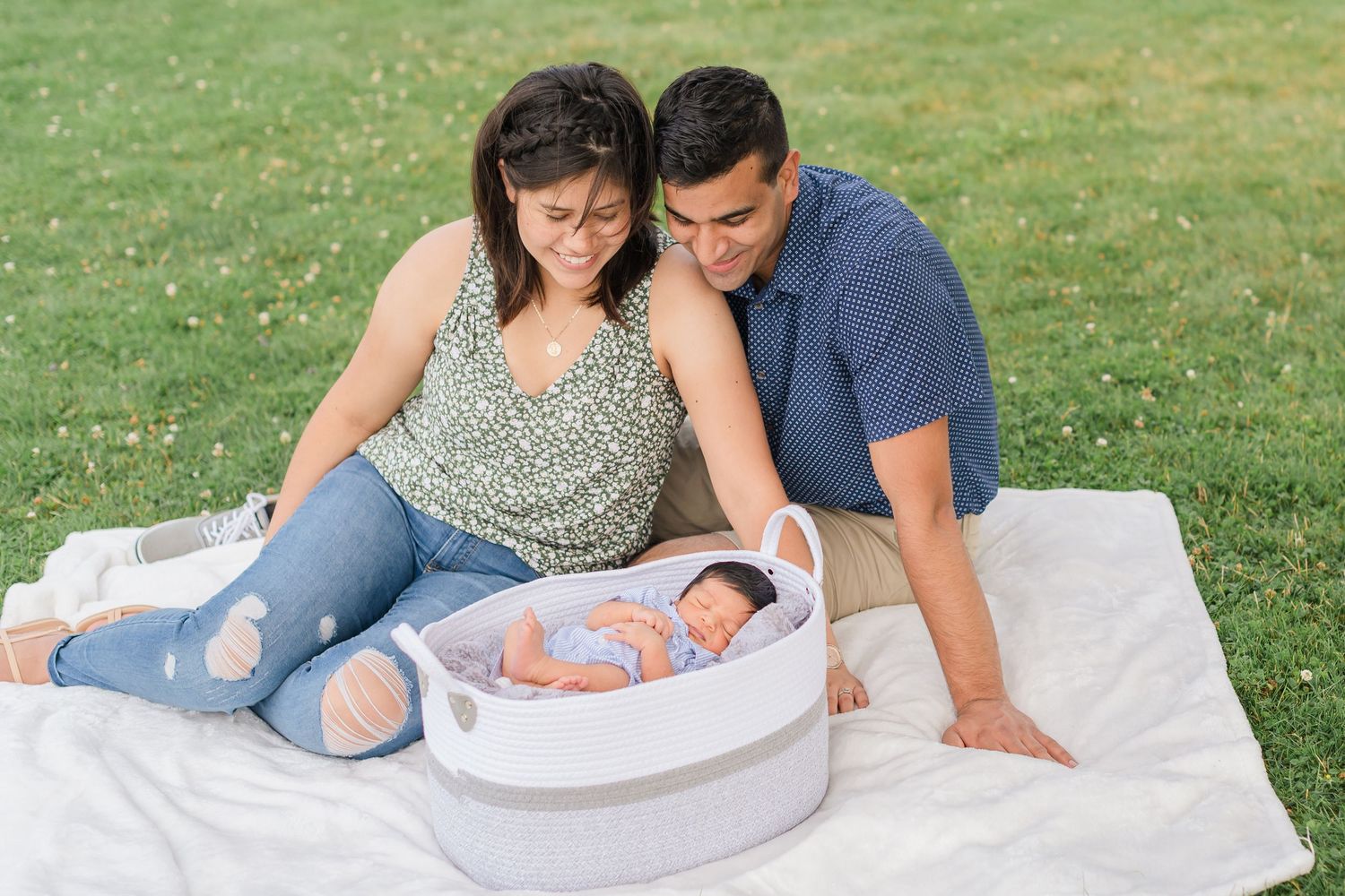 A couple sits together on a blanket in the grass while looking at a white circular object.