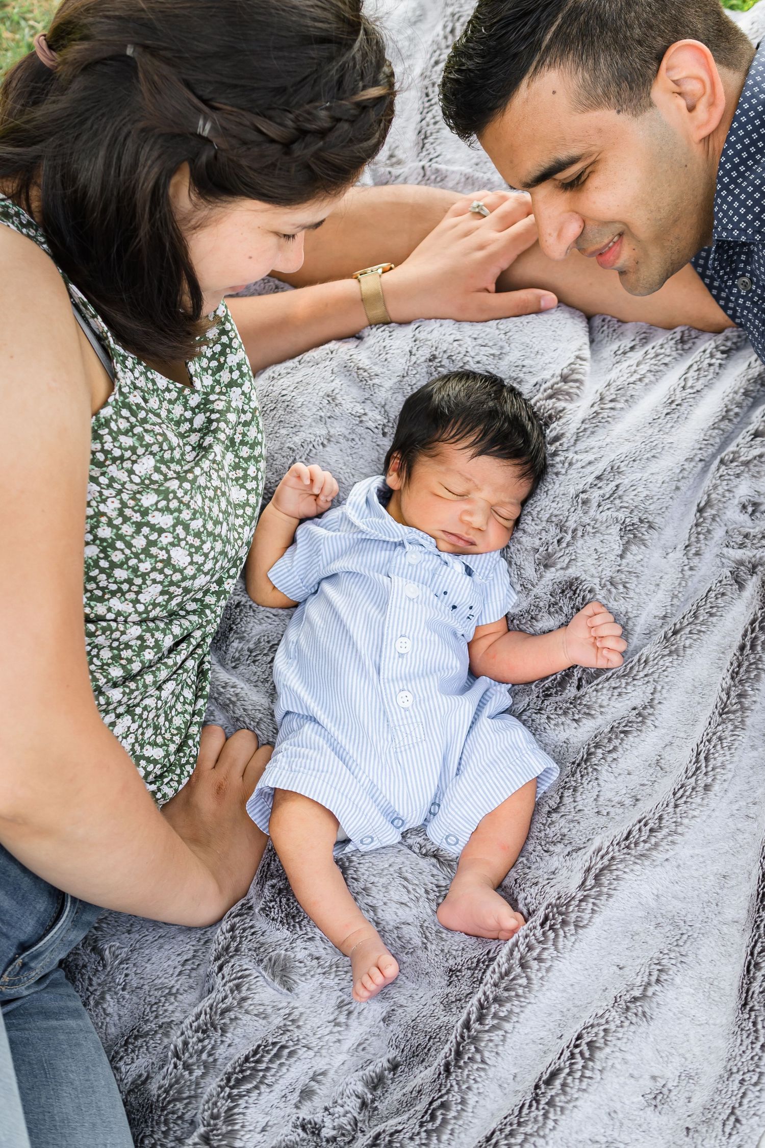 A sleeping newborn baby wearing light blue clothing rests on a gray blanket while being cradled.