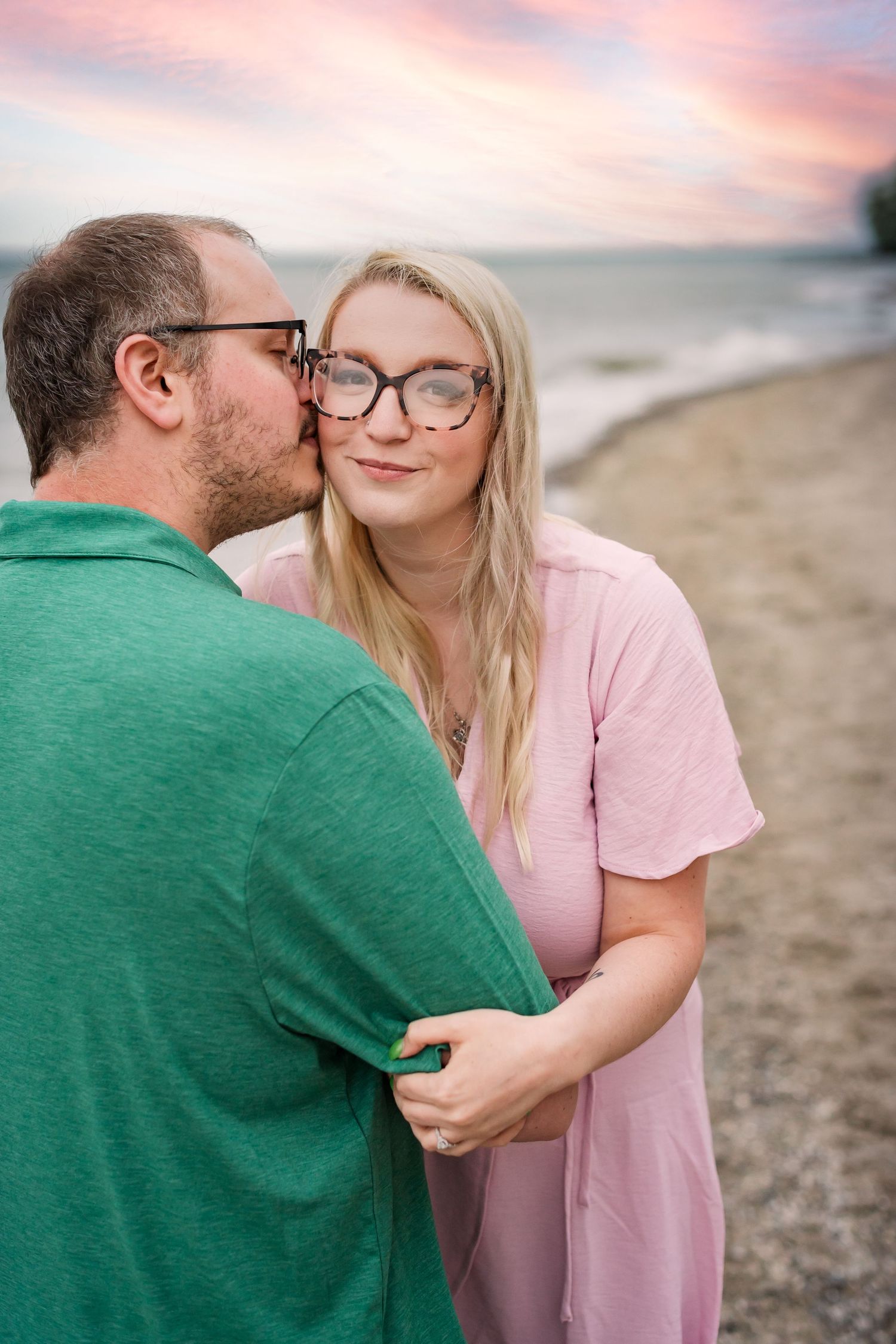 A tender romantic moment shared between a couple in pink and green attire on a sunset beach.