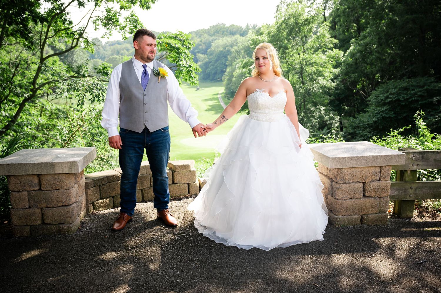 Bride and groom standing on stone overlook with scenic forest view.