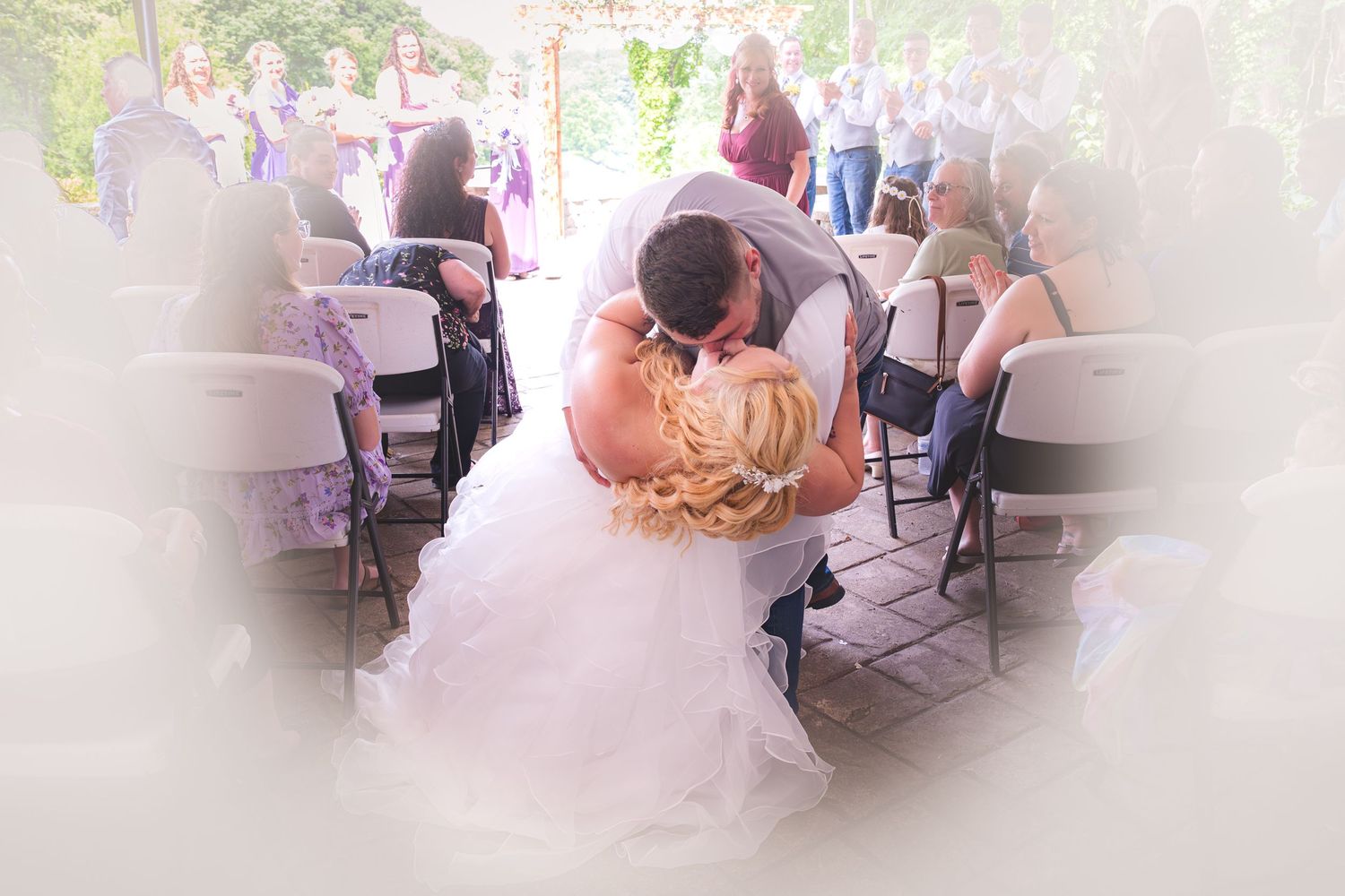 An intimate wedding ceremony view through guests seated in white chairs on an outdoor terrace.
