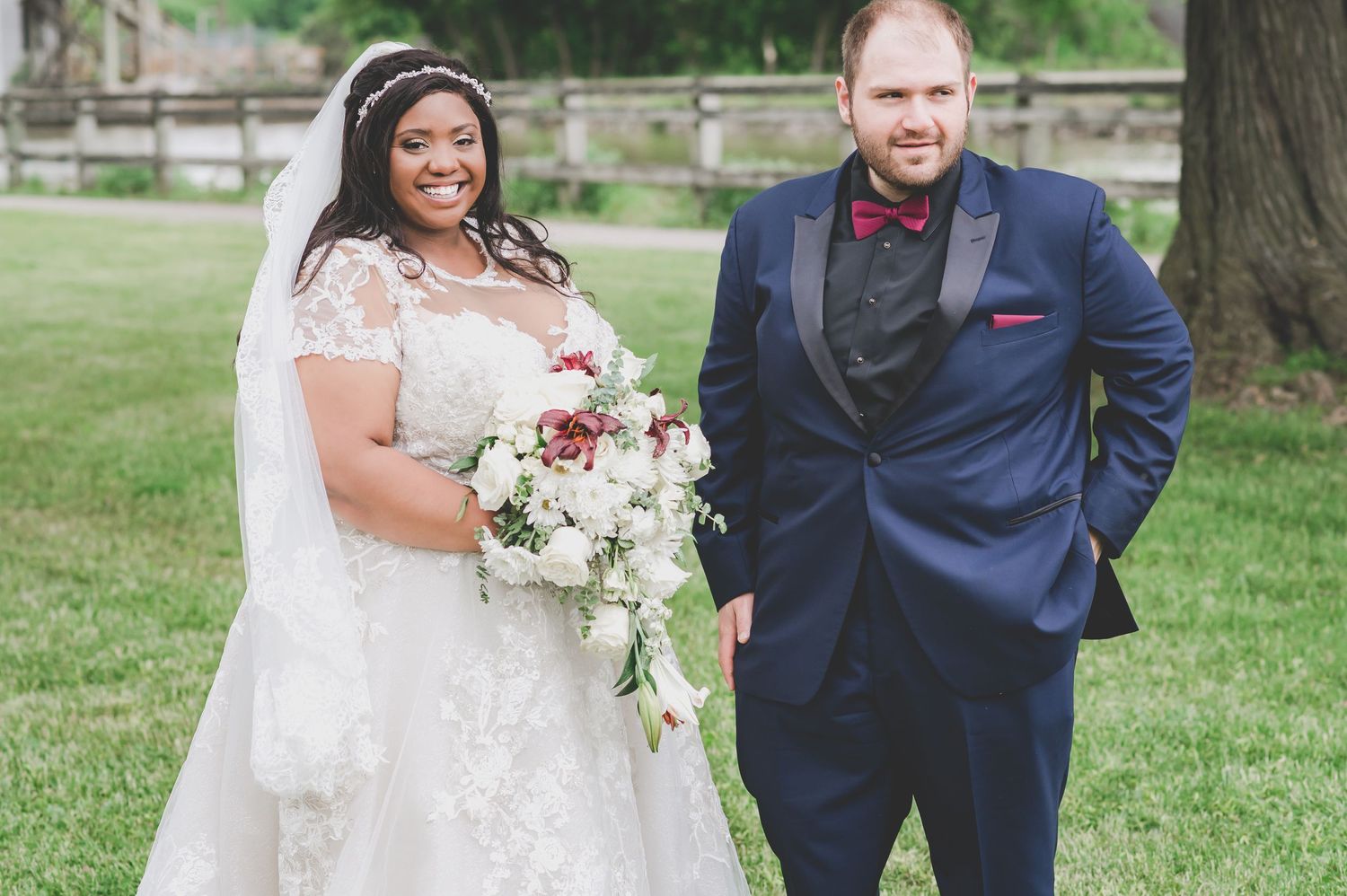 Wedding portrait showcasing elegant bridal bouquet with white and burgundy flowers against natural backdrop.