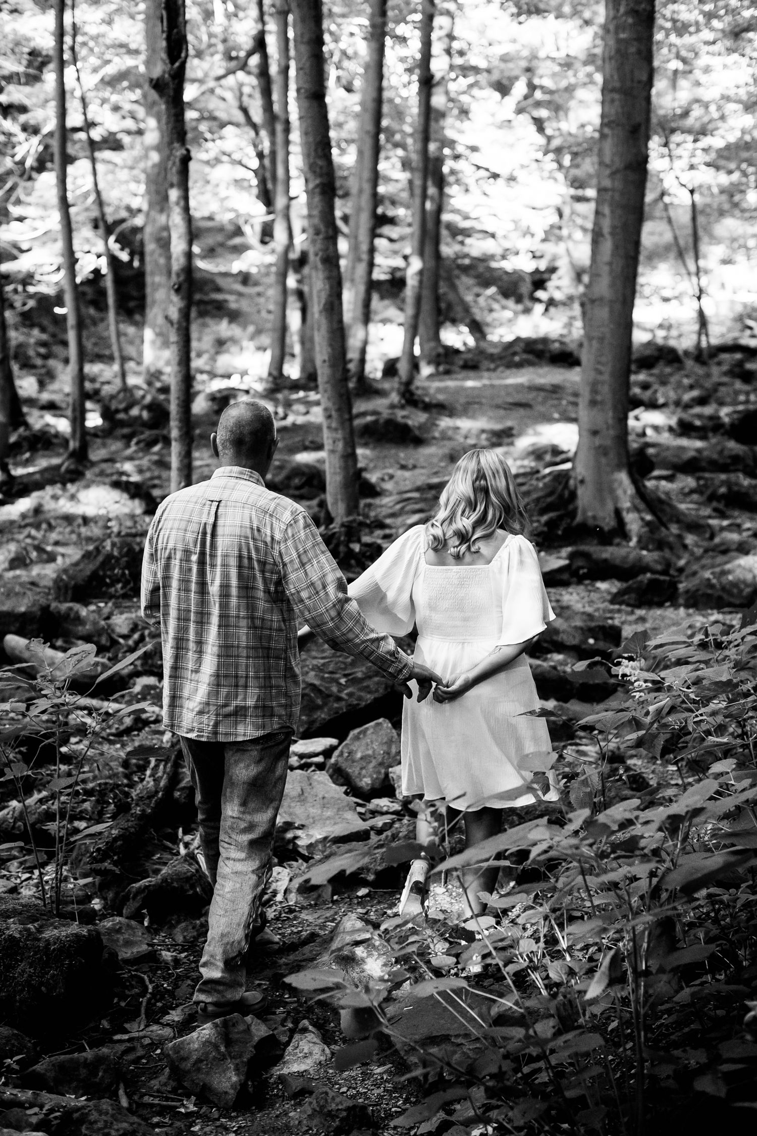 Black and white photo of a couple walking through a rocky forest path holding hands.