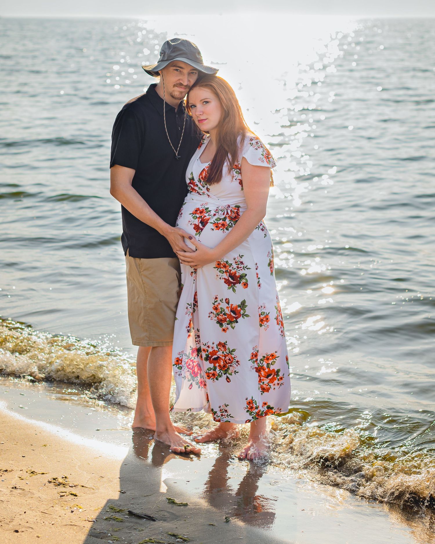 An expectant couple embraces on the beach at sunset during a maternity photoshoot.