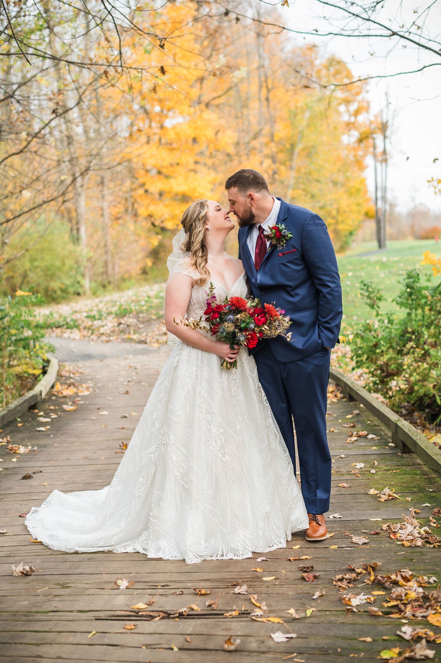 A happy couple shares intimate moments in an autumn setting with fallen leaves and golden foliage on a wooden path.
