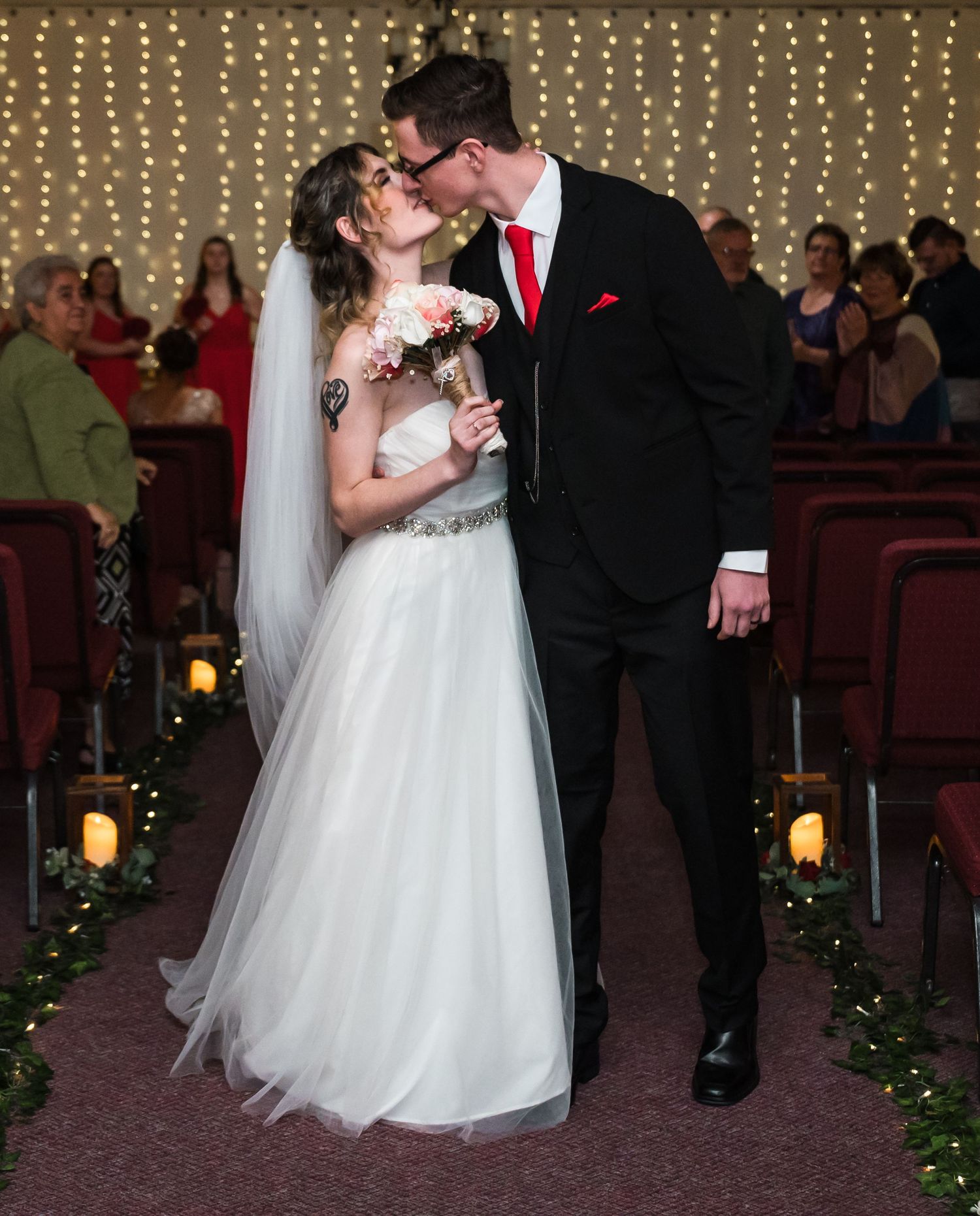 Newlyweds share a romantic candlelit moment in an indoor venue decorated with string lights and lanterns.