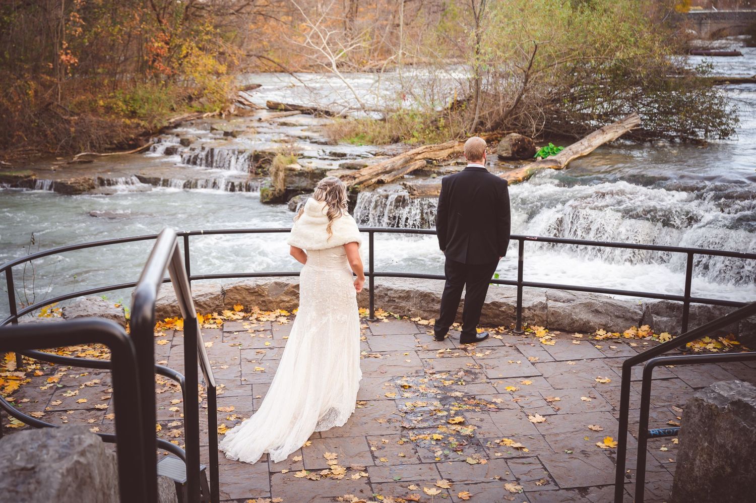 Wedding couple on stone overlook platform with waterfalls and autumn foliage in background.