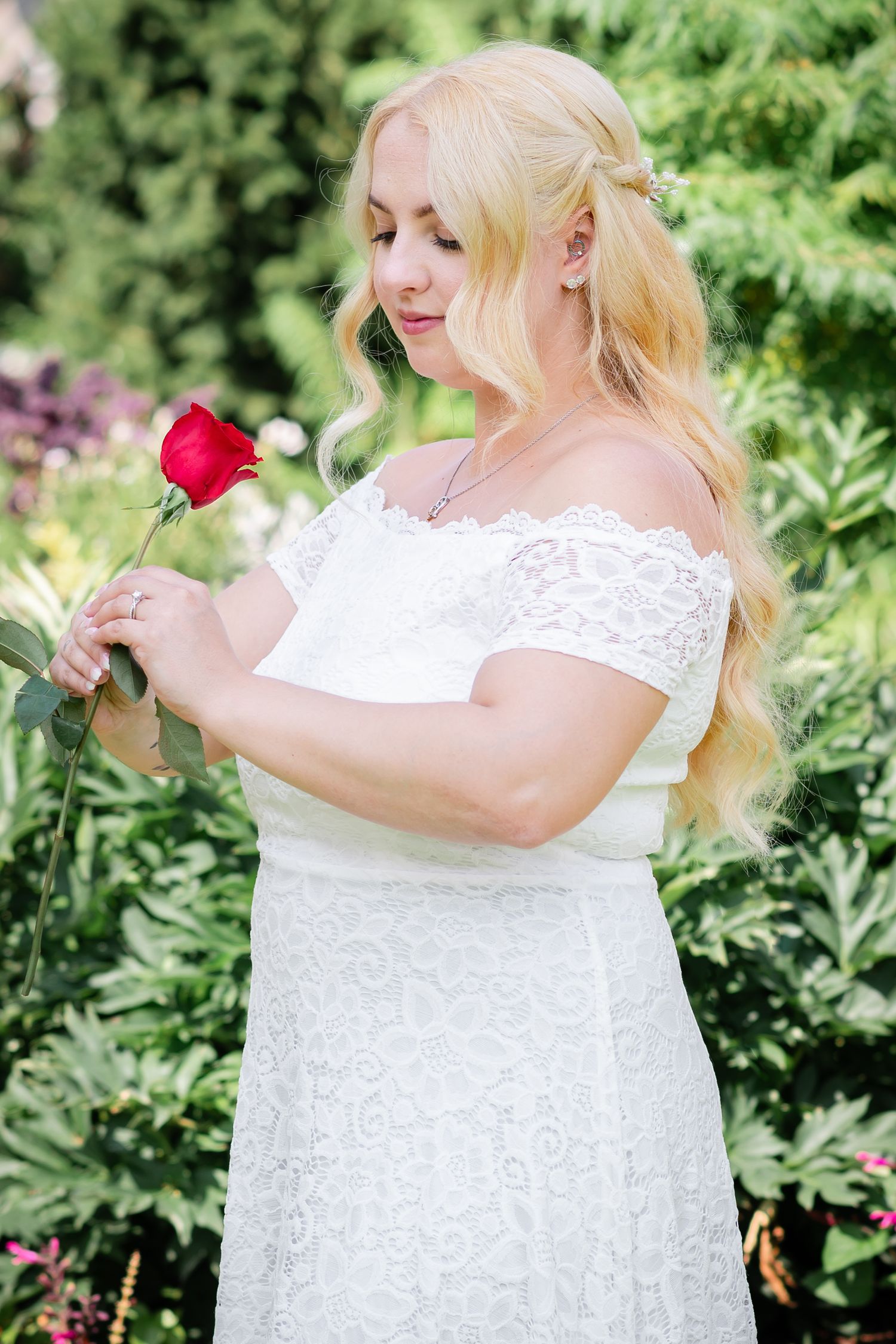 Romantic garden portrait with person in white dress holding red rose.