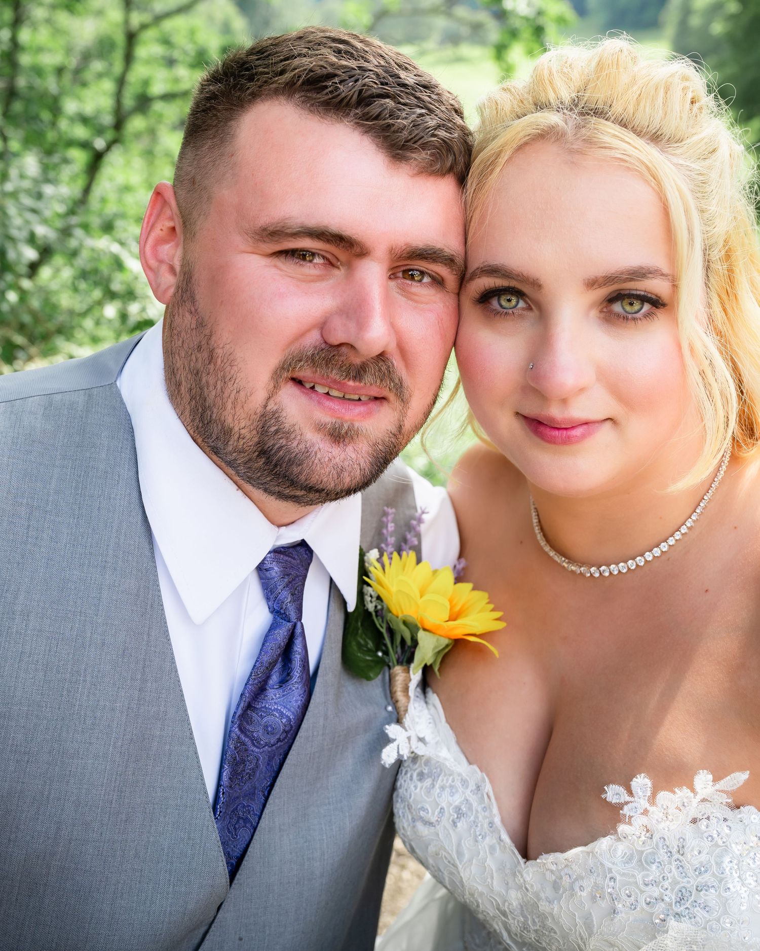 A romantic wedding portrait with a sunflower boutonniere against green foliage.