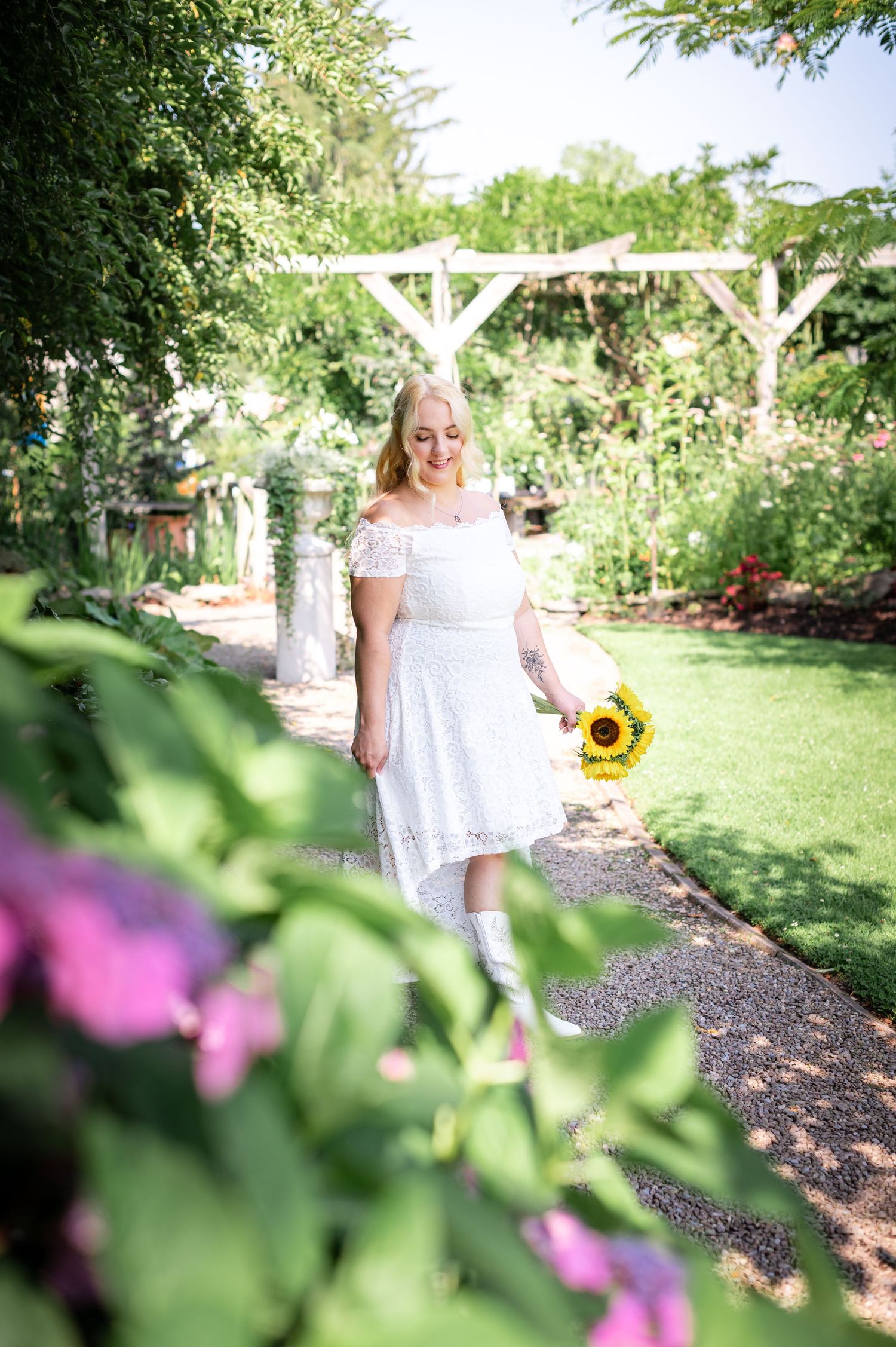 A white dress and sunflower bouquet stand out against a verdant garden backdrop.