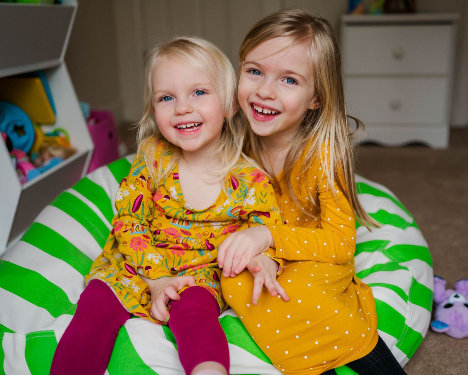 Two children in yellow dresses sit together on a green and white striped bean bag chair.
