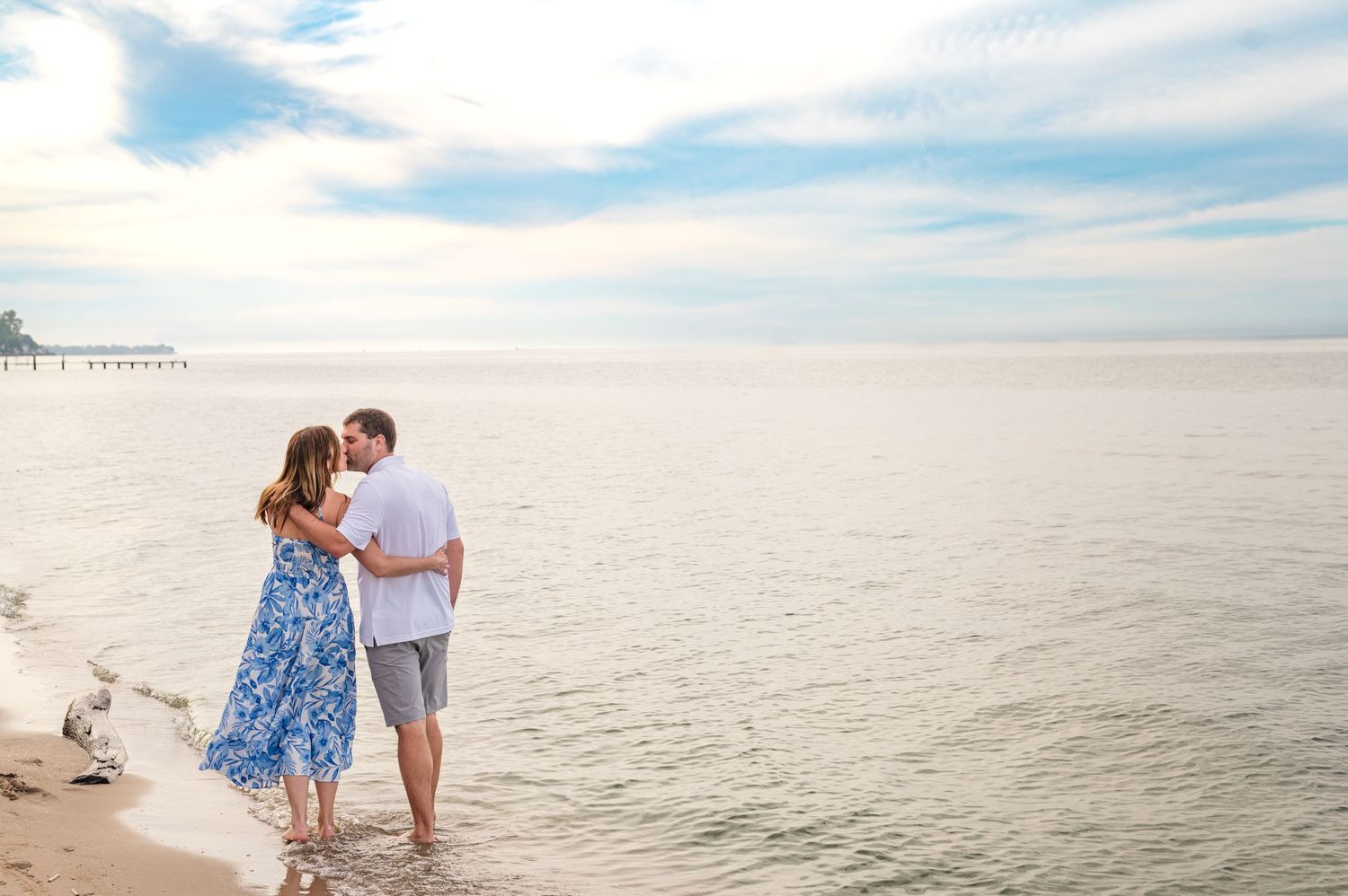 A couple walking along the shoreline in casual beach attire with the ocean in view.