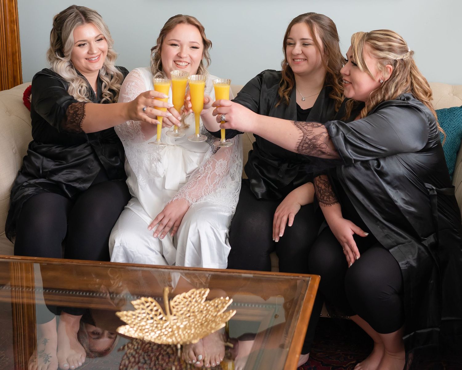 Wedding party in black attire toasting with mimosas around a coffee table.