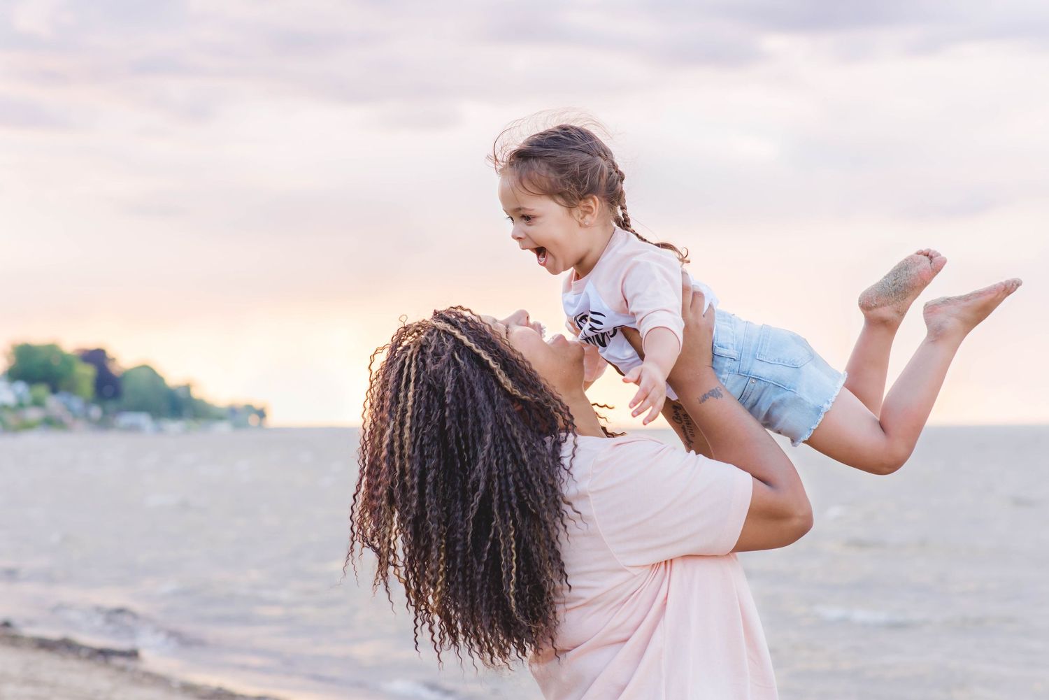 A parent and child share a joyful moment playing together on the beach at sunset.