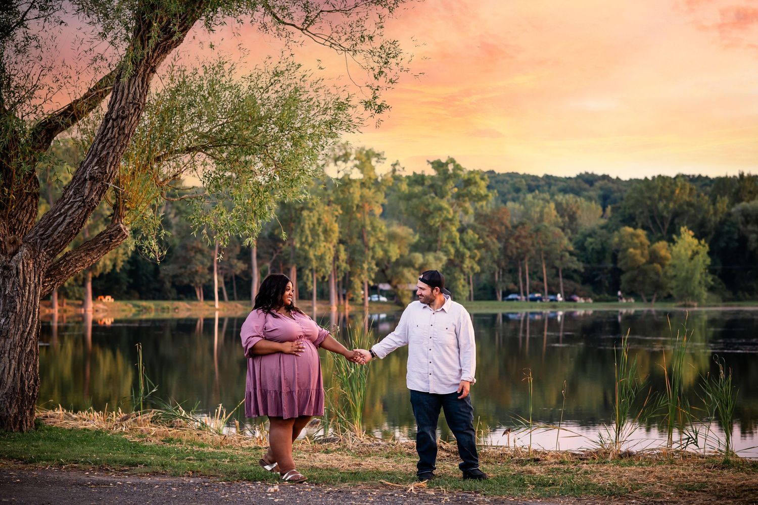 Romantic sunset engagement photo session captured along a tranquil lakeside with trees and golden light.